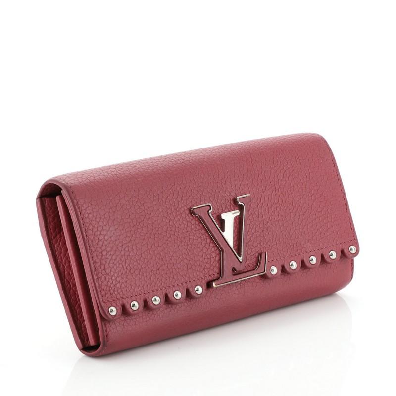 This Louis Vuitton Capucines Wallet Studded Leather, crafted in pink capucines leather, features a signature LV logo in front, stud detailing and silver-tone hardware. Its hidden snap button closure opens to a pink leather interior with multiple