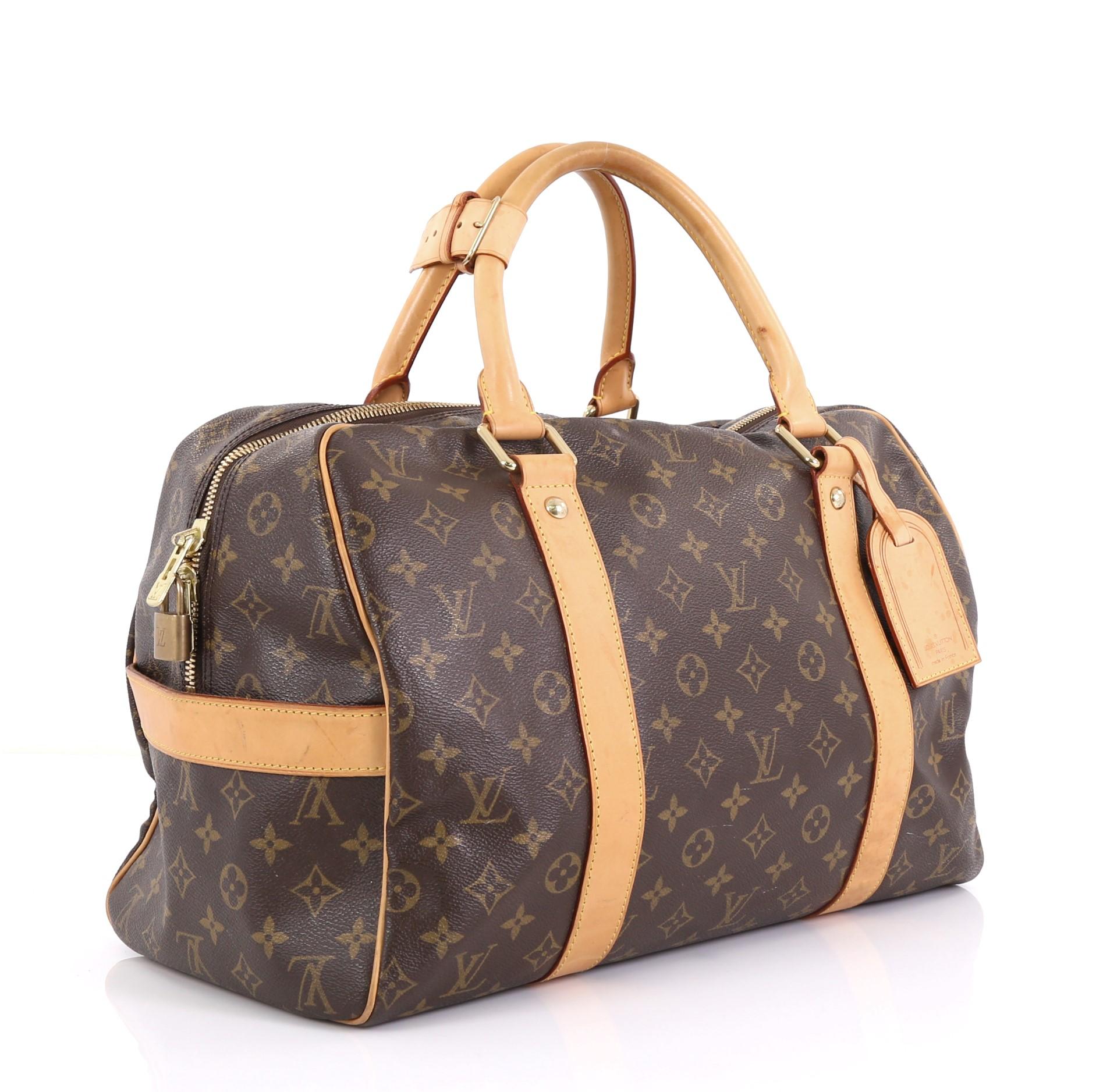 This Louis Vuitton Carryall Handbag Monogram Canvas, crafted in brown monogram coated canvas, features dual rolled handles, cowhide vachetta leather trim, protective base studs, and gold-tone hardware. Its top zip closure opens to a brown fabric
