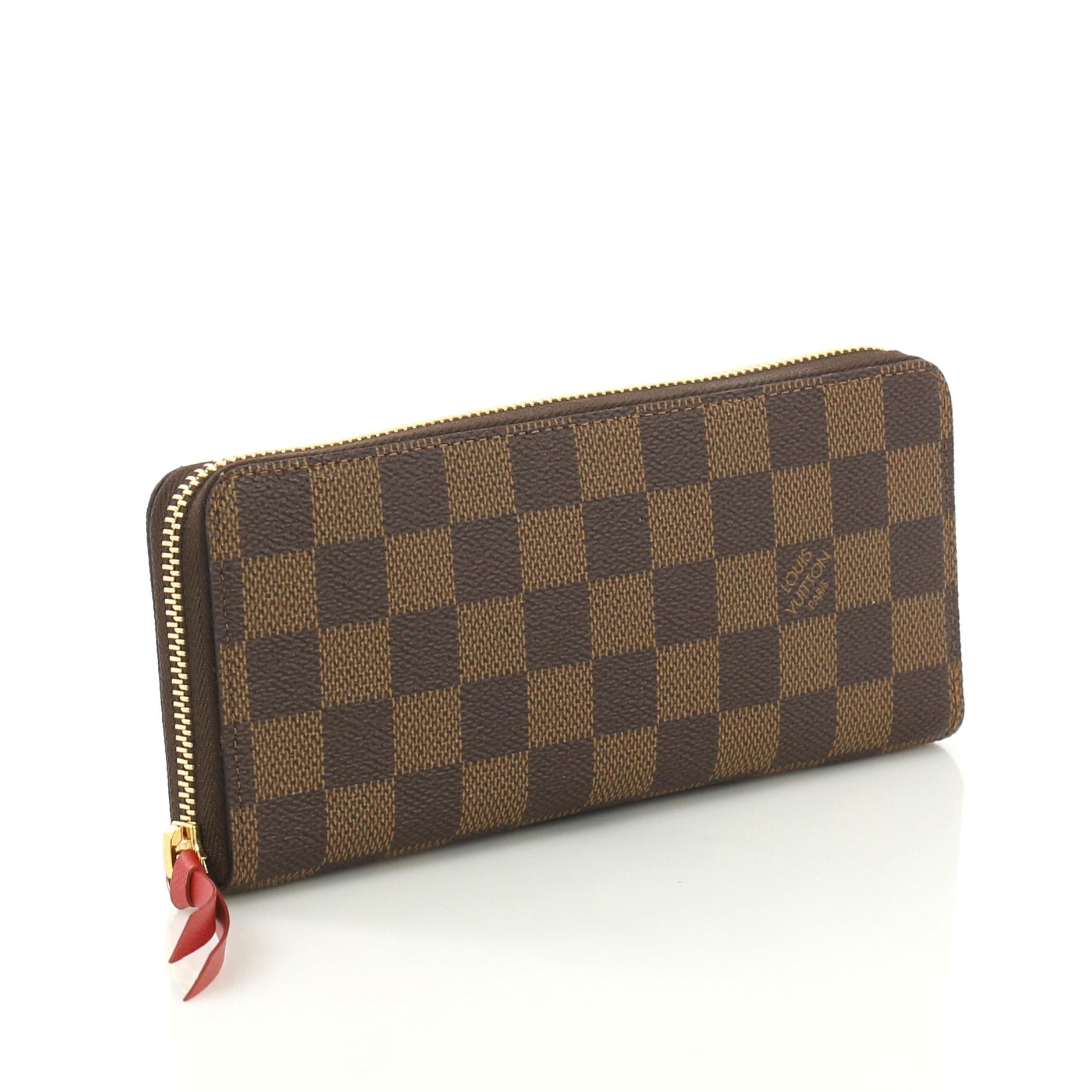 This Louis Vuitton Clemence Wallet Damier, crafted from damier ebene coated canvas, features gold-tone hardware. Its all-around zip closure opens to a red leather interior with multiple card slots, slip pockets, gusseted compartments and middle zip