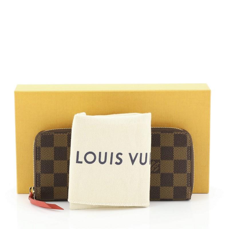 This Louis Vuitton Clemence Wallet Damier, crafted from damier ebene coated canvas, features gold-tone hardware. Its all-around zip closure opens to a red leather interior with multiple card slots, two gusseted open pockets, and zip pocket.