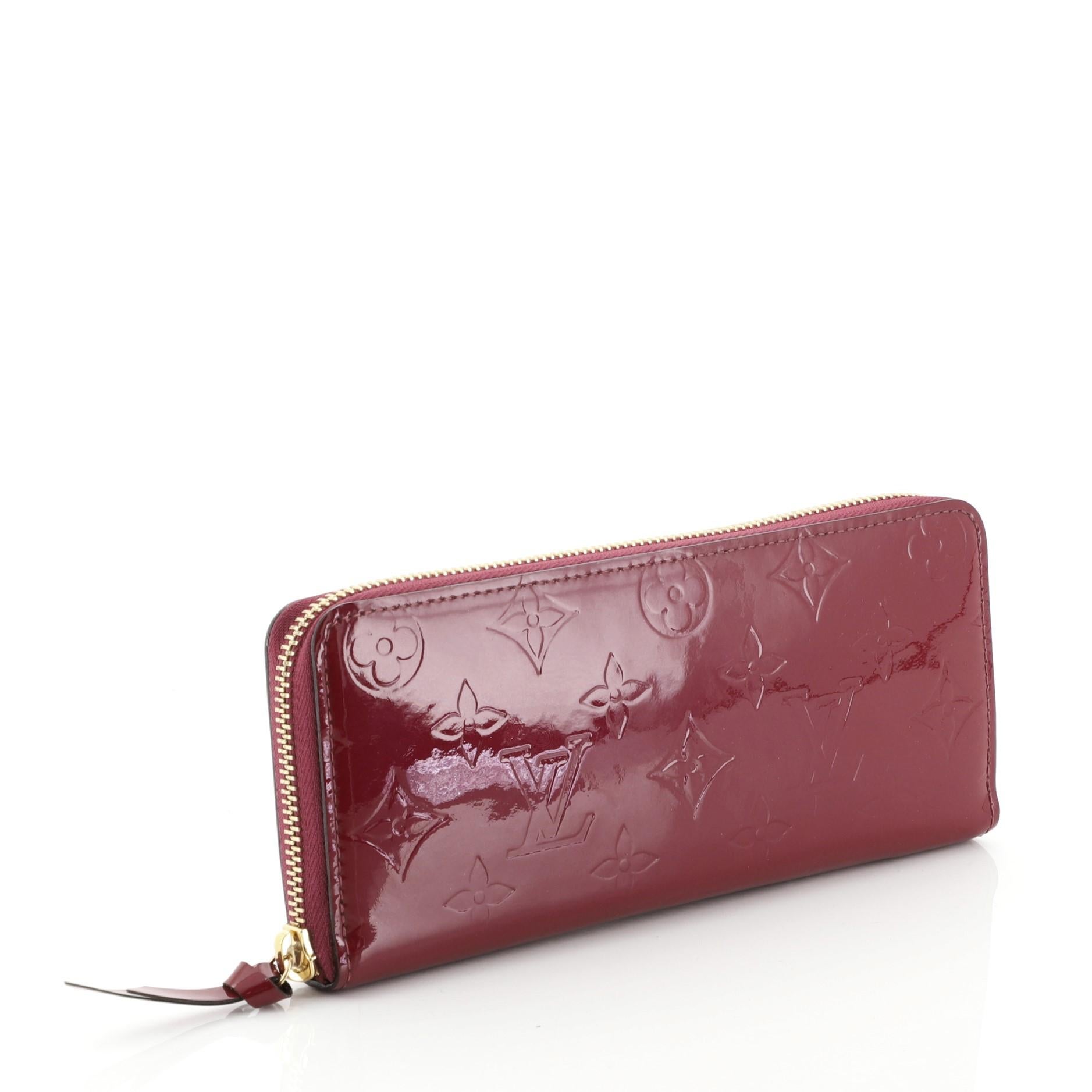 This Louis Vuitton Clemence Wallet Monogram Vernis, crafted from purple monogram vernis, features gold-tone hardware. Its all-around zip closure opens to a purple leather interior with multiple card slots, slip pockets, gusseted compartments, and