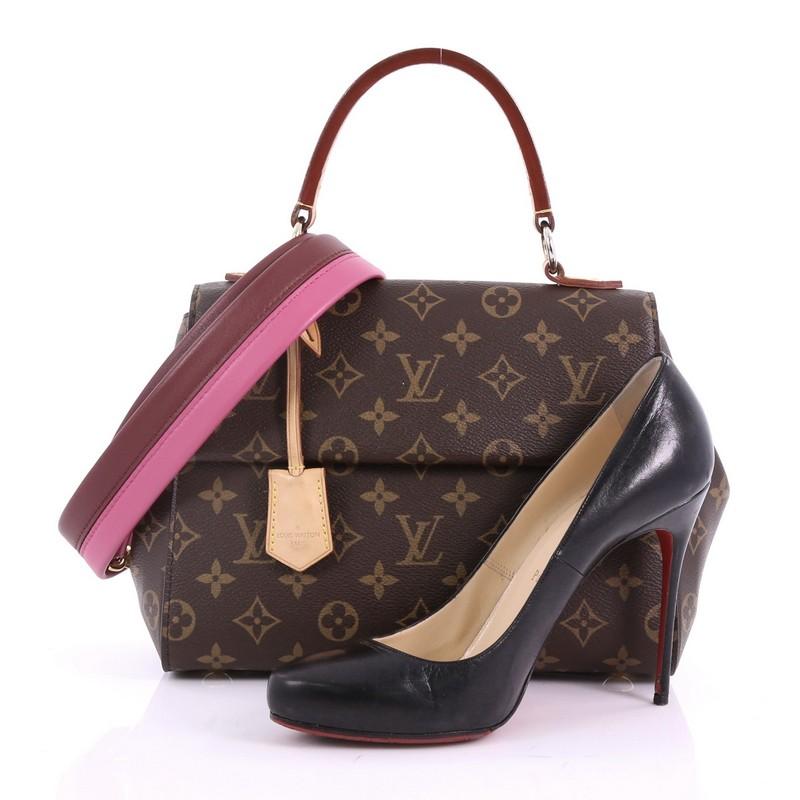This Louis Vuitton Cluny Top Handle Bag Monogram Canvas BB, crafted in brown monogram coated canvas, features a leather top handle, protective base studs, and gold-tone hardware. Its magnetic closure opens to a pink fabric interior with zip and slip