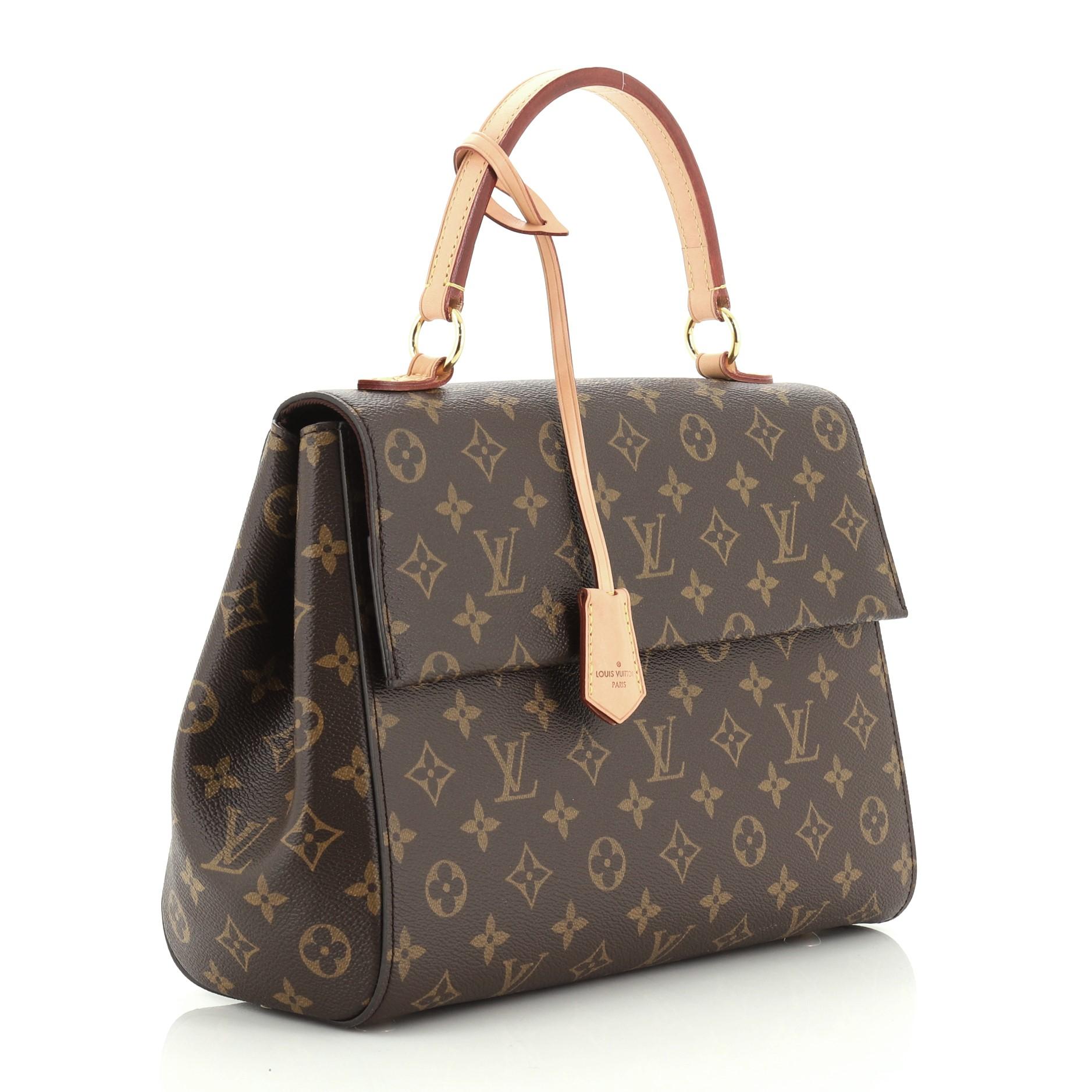 This Louis Vuitton Cluny Top Handle Bag Monogram Canvas MM, crafted in brown monogram coated canvas, features a leather top handle, colored detachable strap, front flap, protective base studs, and gold-tone hardware. Its magnetic closure opens to a
