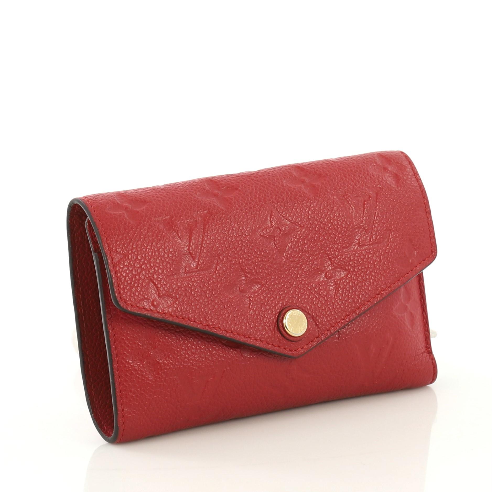 This Louis Vuitton Compact Curieuse Wallet Monogram Empreinte Leather, crafted from red monogram empreinte leather, features frontal flap and gold-tone hardware. Its press button closure opens to a red leather interior with multiple card slots,