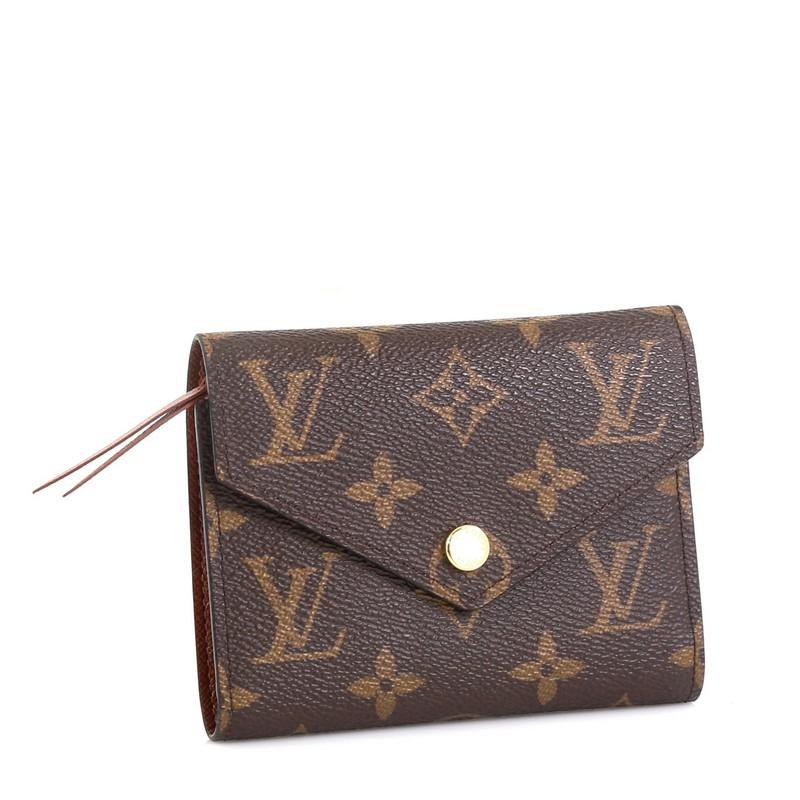 This Louis Vuitton Compact Victorine Wallet Monogram Canvas, crafted in brown monogram coated canvas, features gold-tone hardware. Its press-stud closure opens to a brown leather interior with multiple card slots, zip pocket and bill pocket.