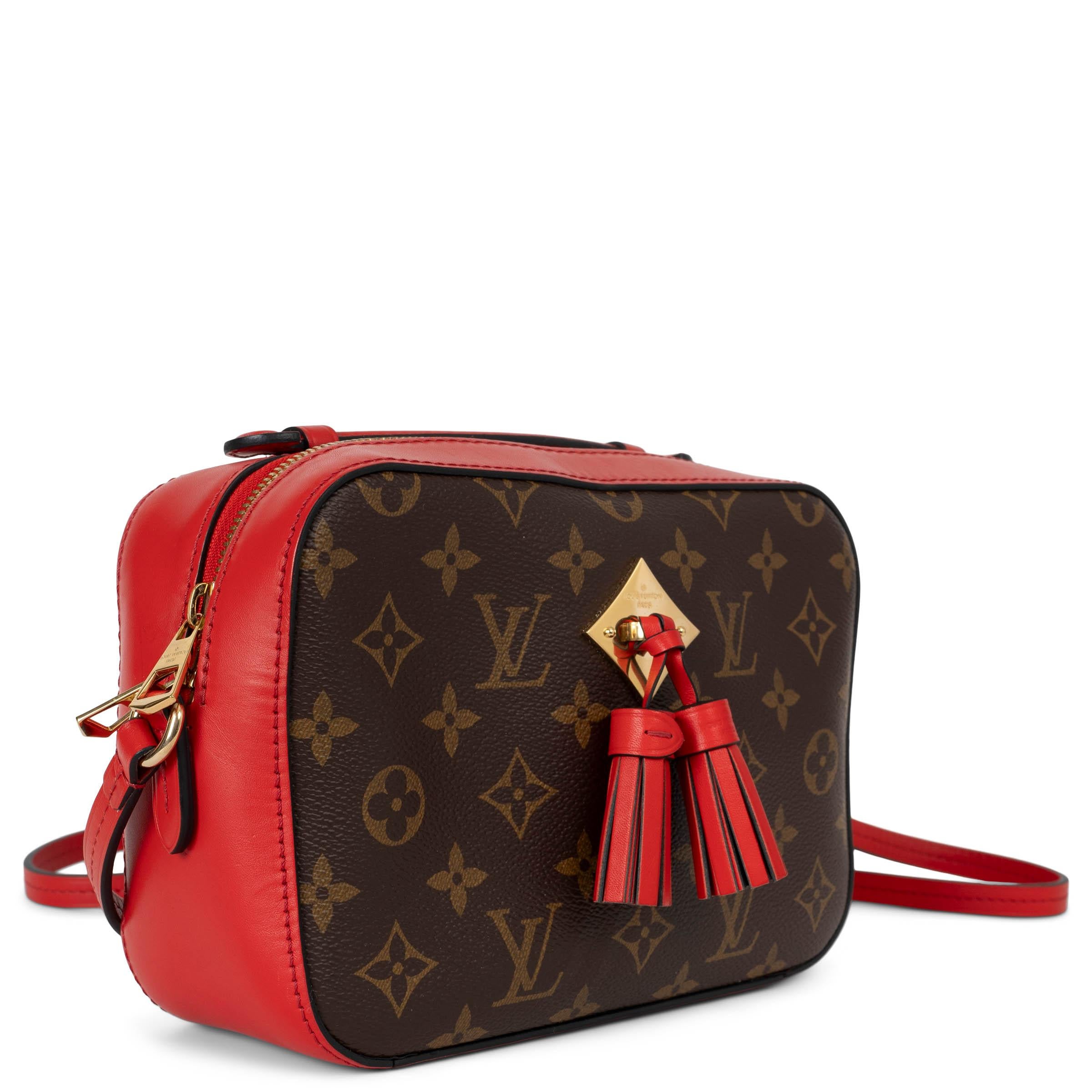 This 100% authentic Louis Vuitton Saintonge crossbody camera bag combines Ebene brown Monogram canvas with vibrant Coquelicot red leather trims for a striking look. It features a gold-tone logo-engraved metal plate on the front, accented with two