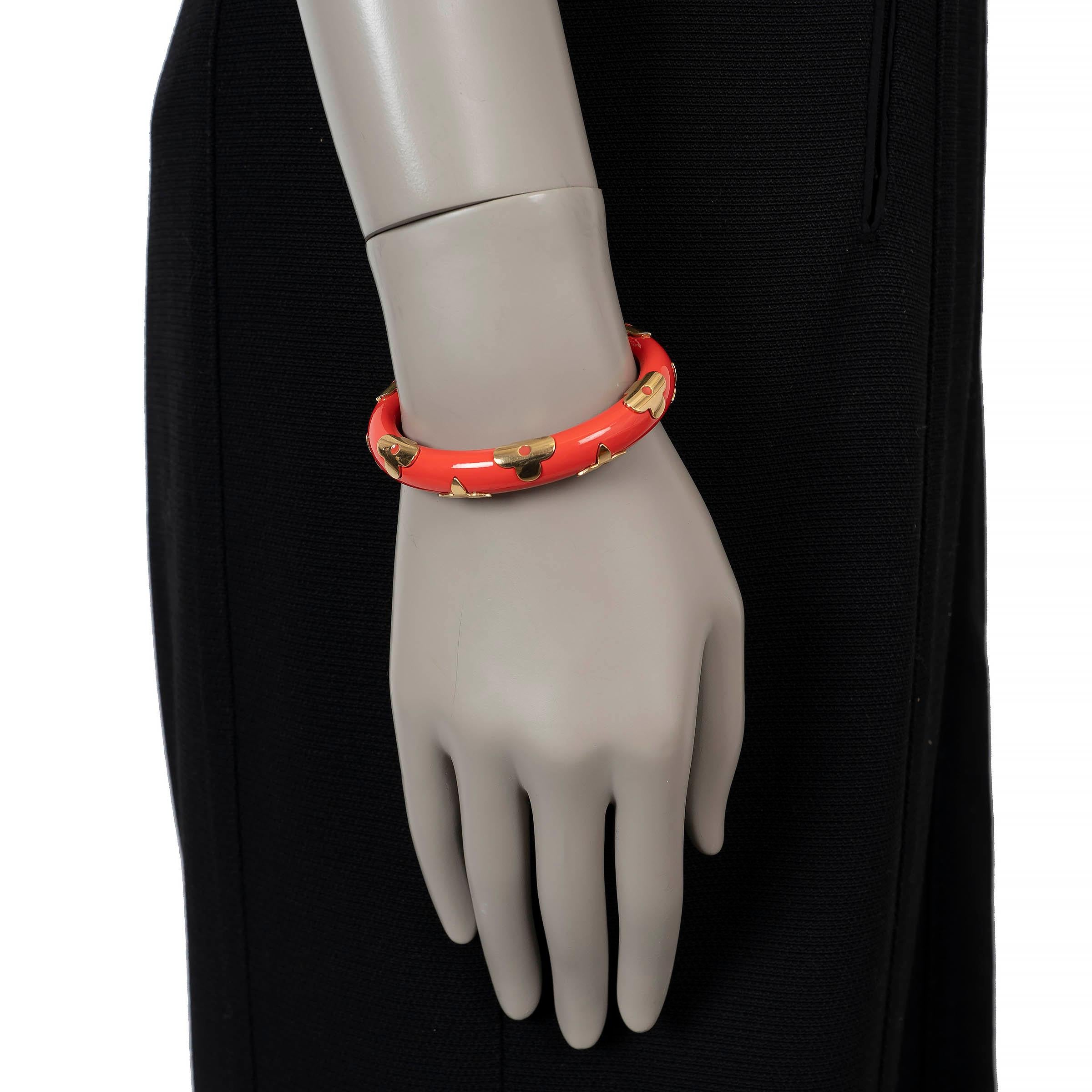 This 100% authentic Louis Vuitton Daily Monogram cuff bracelet is crafted from glossy coral enamel and finished with gold-tone Monogram flower and LV logo motifs. The open cuff design offers an effortless slip-on fit, while the bold color and