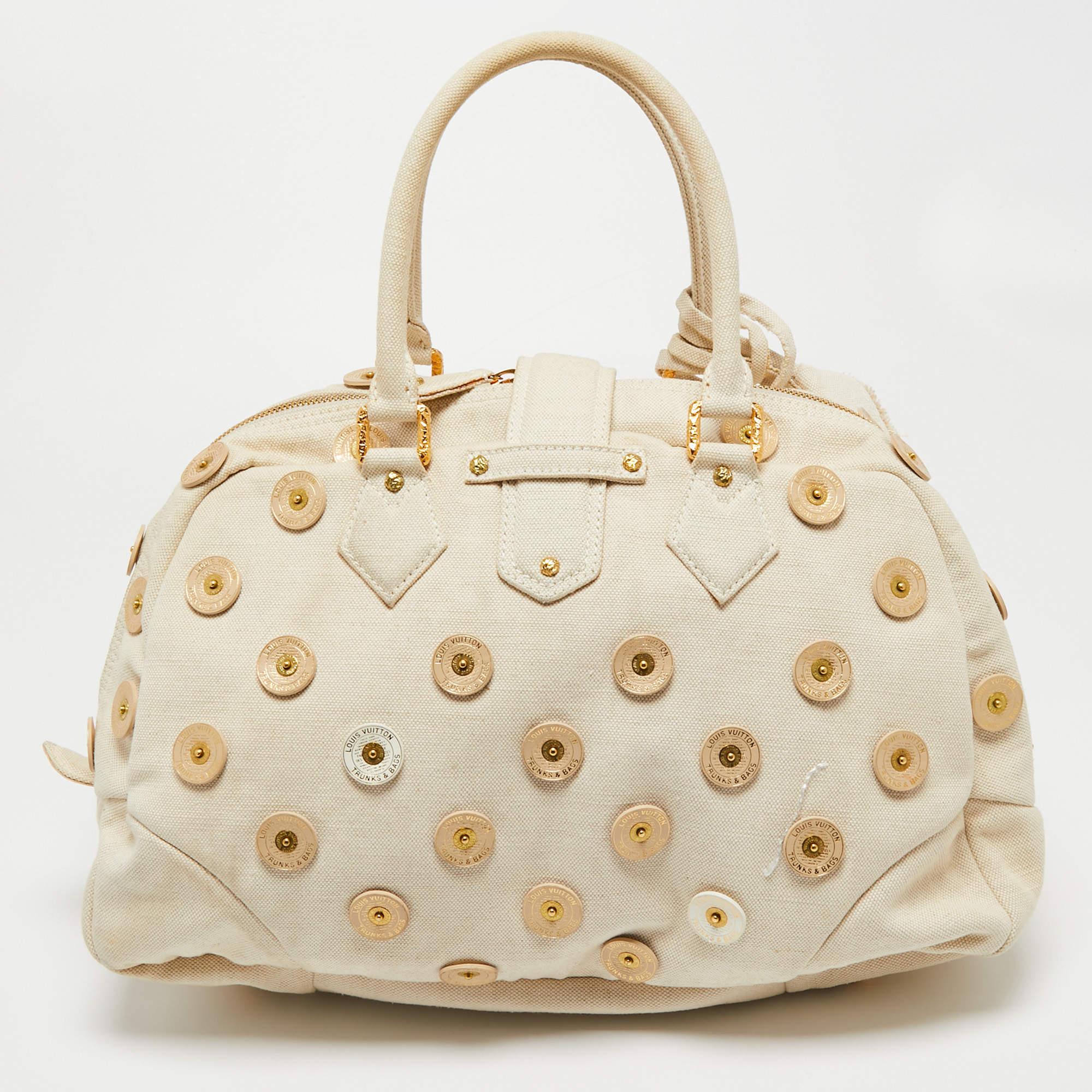 Louis Vuitton's handbags are popular owing to their high style and functionality. Crafted from cream canvas, this Panama Bowly bag has a beautiful polka dot design all over. The pretty bag features dual top handles, tags, a textured S lock, and a