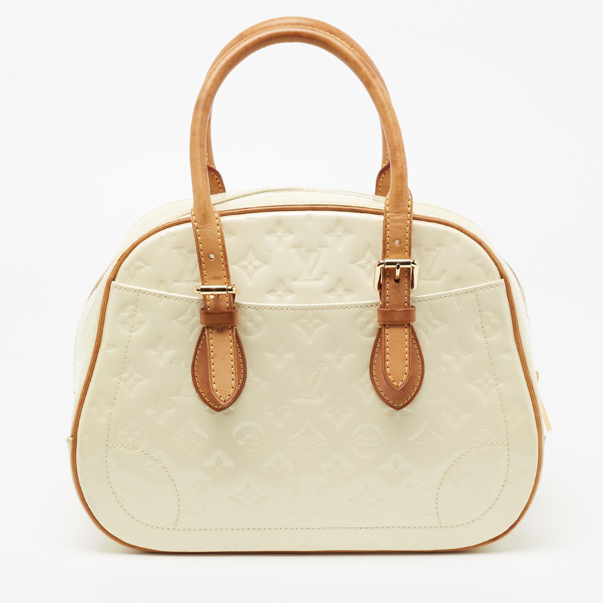 Well-made and essaying luxury, this Louis Vuitton bag will take you through your day with ease. Crafted from cream Monogram Vernis, it features dual handles and exterior slip pockets. The bag is secured by a wide two-way zip closure that opens to a