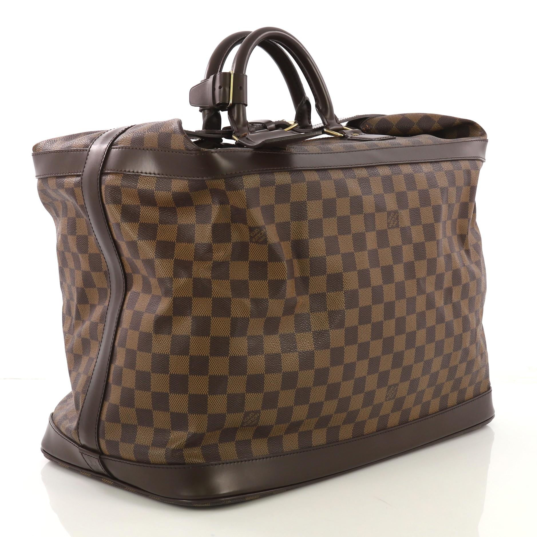 This Louis Vuitton Cruiser Handbag Damier 45, crafted in damier ebene coated canvas, features dual rolled handles, dark brown leather trim, and gold-tone hardware. Its top buckle belt strap and zip closure holds the folded top of the bag and opens