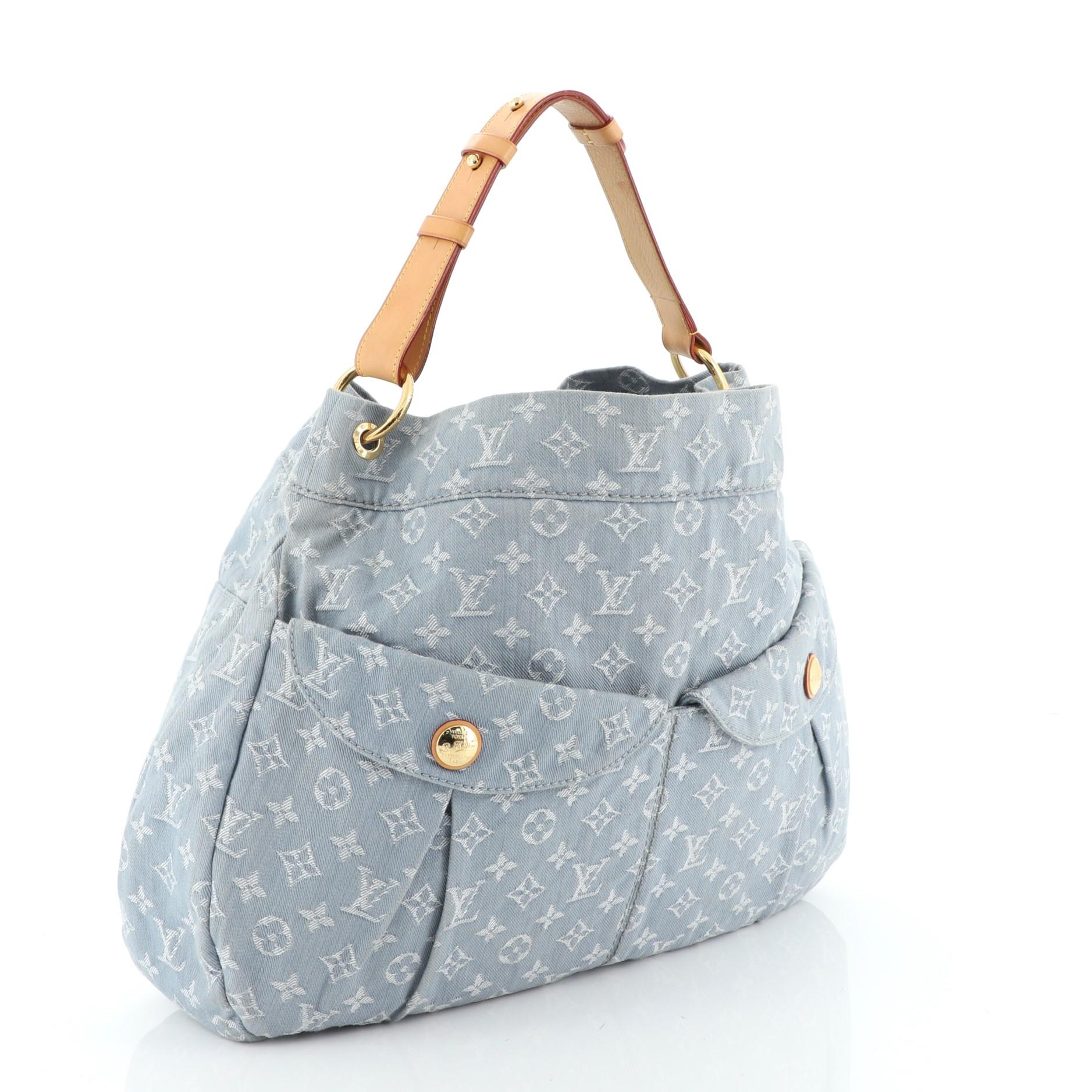 This Louis Vuitton Daily Handbag Denim GM, crafted from blue denim, features an adjustable vachetta leather shoulder strap, two exterior front pockets with snap button closure, and gold-tone hardware. Its hook closure opens to a gray microfiber