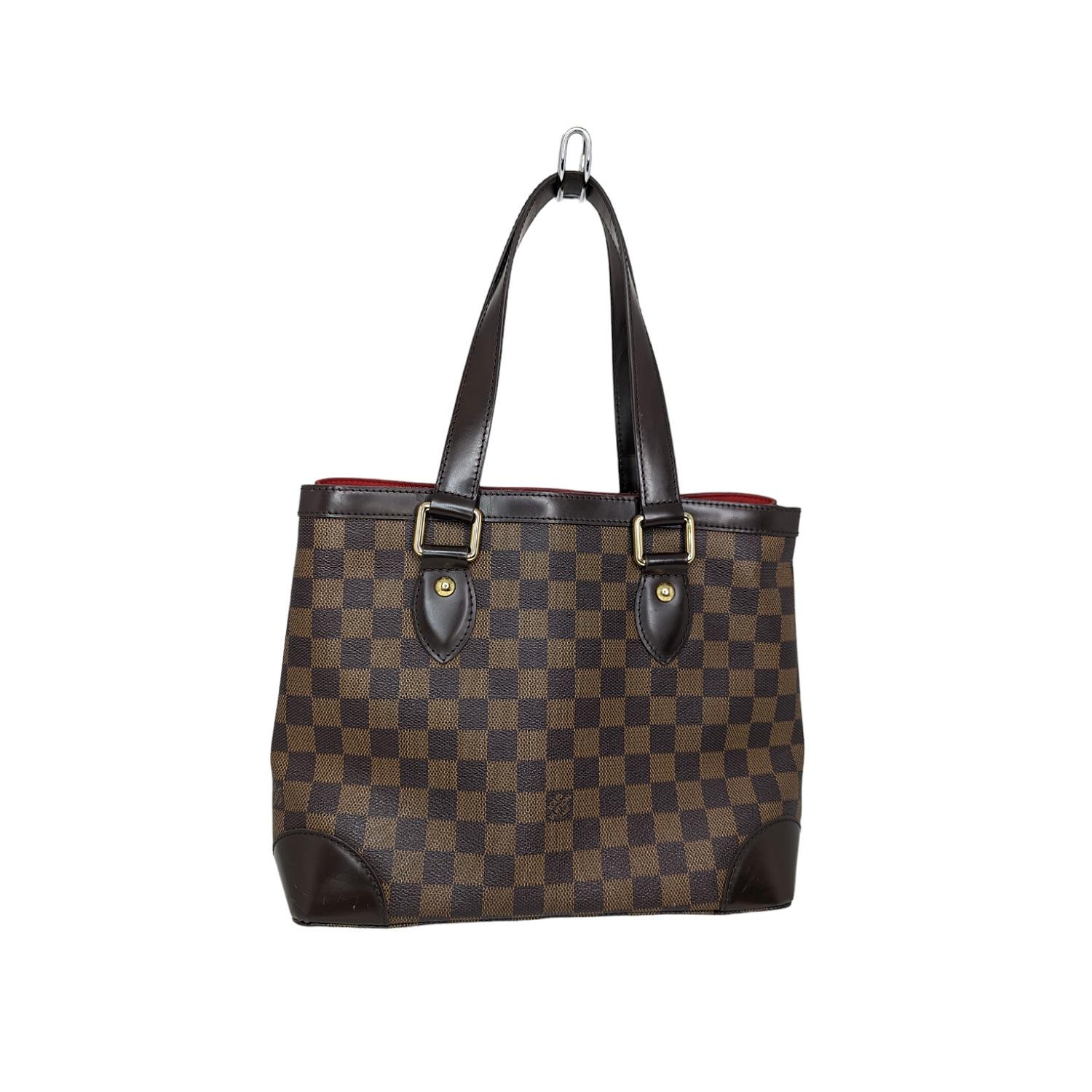 This Louis Vuitton Damier Canvas Hampstead Bag is a spacious classic tote made in Damier Ebene print, which pairs classic canvas with a smooth leather accent. With its expandable sides and roomy capacity, it will hold all your daily essentials in