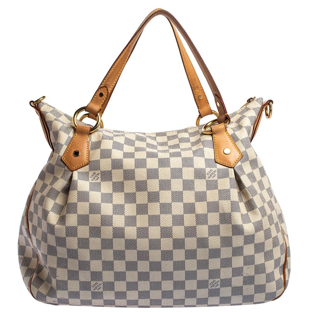 Designed with the classic Damier Azur print, this Louis Vuitton Evora tote is convenient and sophisticated. It features luxurious tan leather trim with double top handles and an adjustable shoulder strap with a gold-tone buckle matching the front