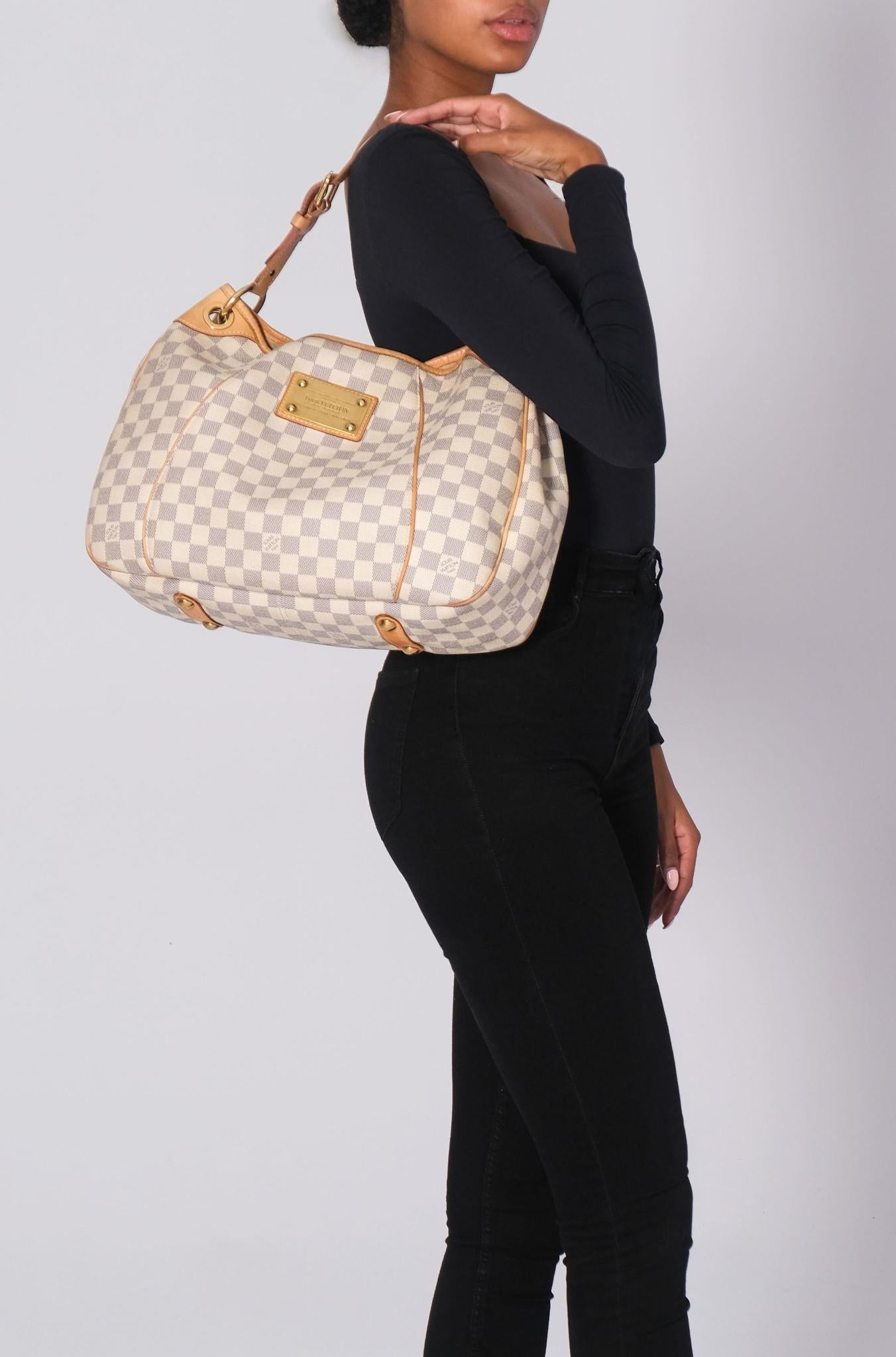 This hobo style bag is made of Louis Vuitton's signature Damier canvas in blue and white. It features a vachetta cowhide leather adjustable looping shoulder strap, piping trim, and polished brass hardware. The top opens to a beige microfiber