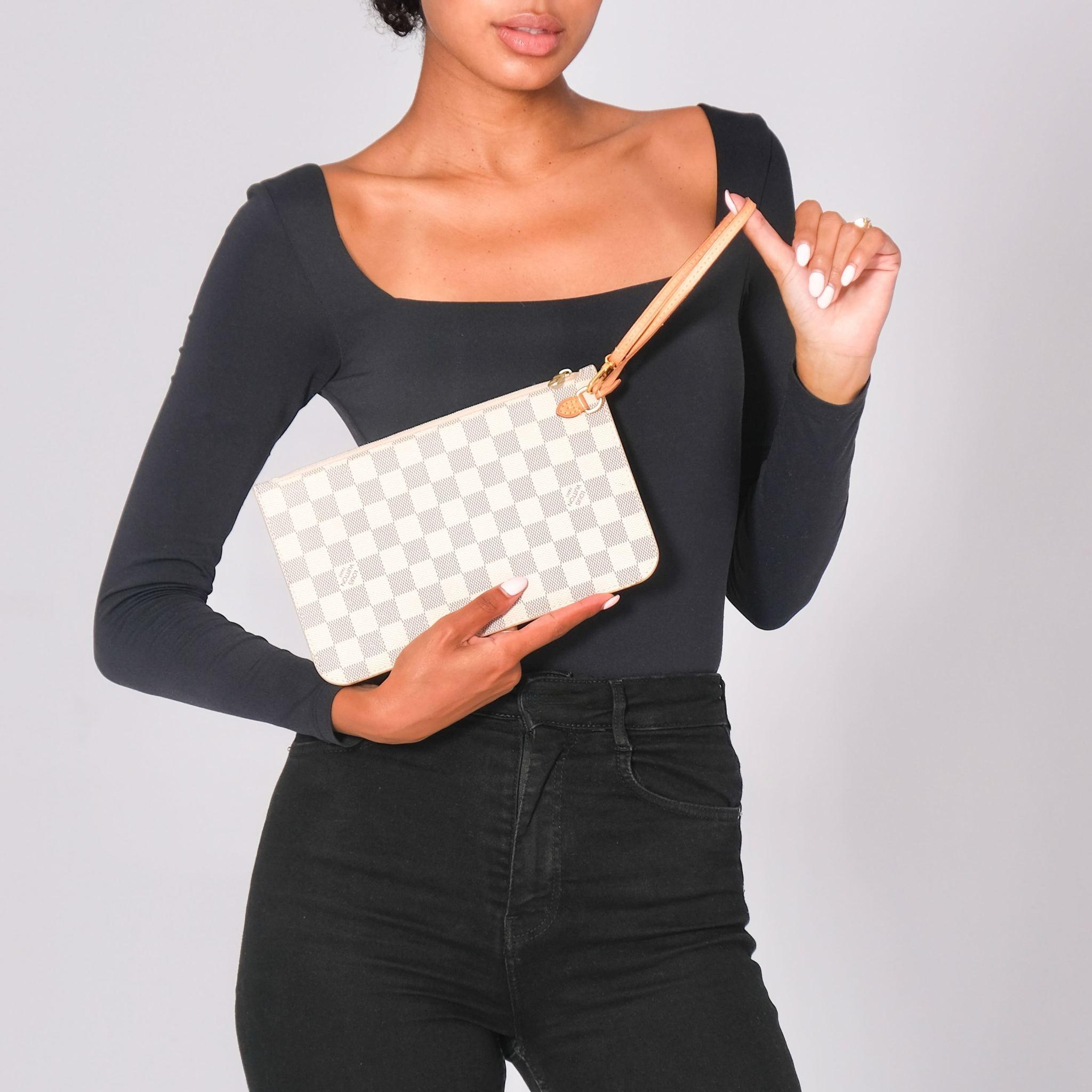 This pouch bag is made of Louis Vuitton Damier Azur canvas in blue and white with a rose pink striped interior. It features a vachetta cowhide leather strap, a lobster clasp on the strap to secure it in a larger bag, gold-tone hardware, a top zip