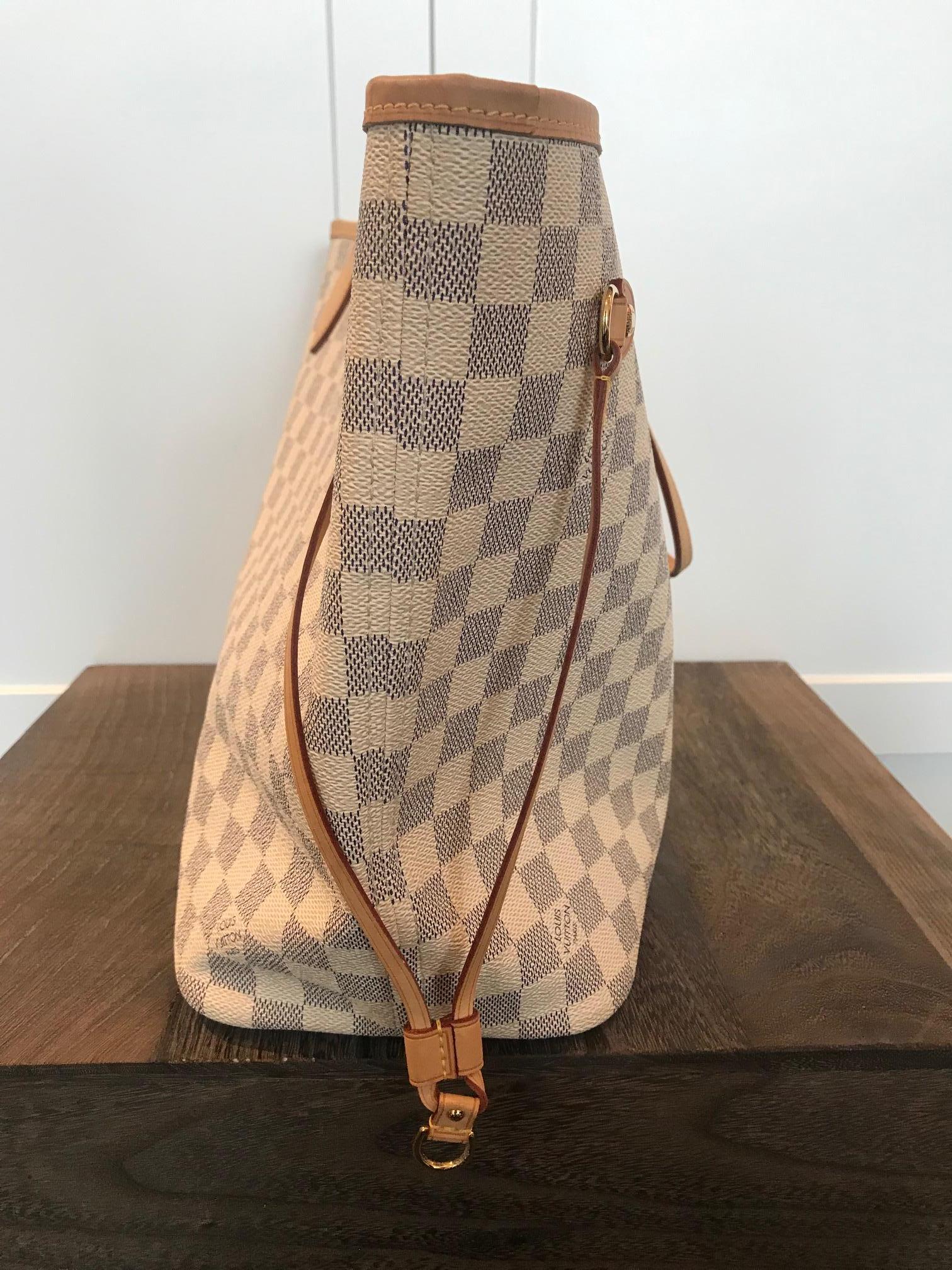 Creme and navy Damier Azur coated canvas. Brass hardware. Clasp closure at top. Dual flat shoulder straps. Tan Vachetta trim. Dual drawstring accents at sides. Creme and beige stripe print woven lining. One interior zippered pocket.