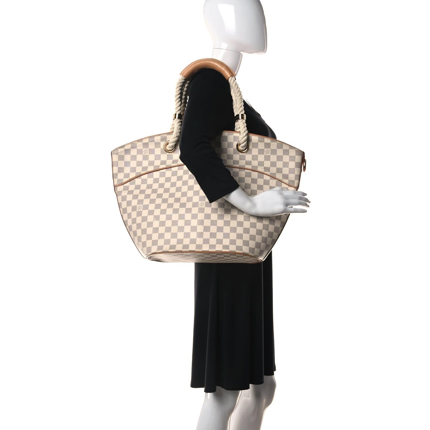 This tote is made of Louis Vuitton damier azur check toile canvas. The bag features vachetta cowhide leather trim and rope top handles with vachetta grips. The top opens to vachetta trim and a beige fabric interior with zipper and patch