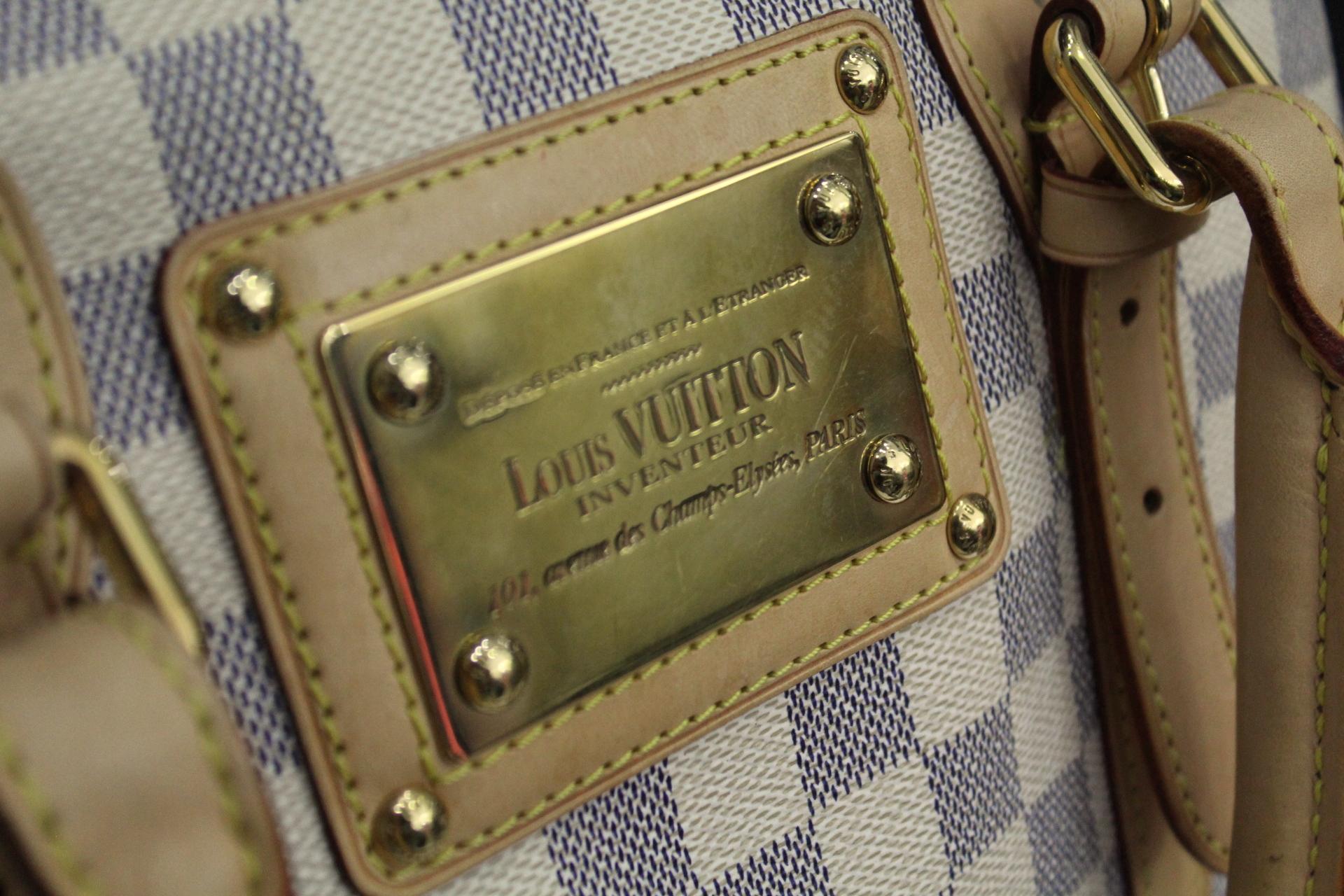  This wonderful day bag is crafted of signature azur damier Louis Vuitton patterned canvas with complimentary vachetta cowhide leather including corner plates and rolled leather adjustable top handles. There is polished brass including buckles and a