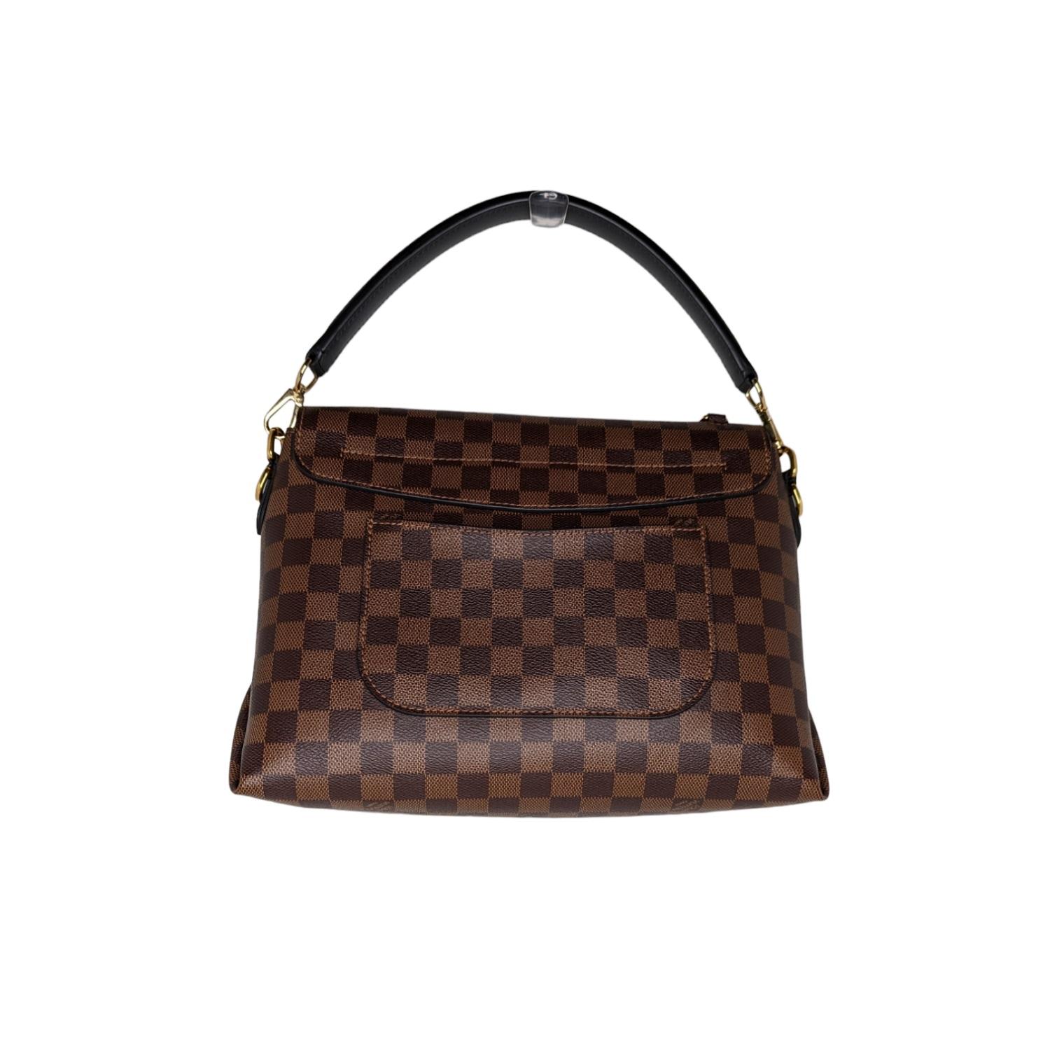 This stylish bag is crafted of Louis Vuitton Damier Ebene coated canvas. The bag features a flat strap top handle, an optional shoulder strap, a rear pocket, and polished gold hardware. The bag has an envelope style flap that leads to a black