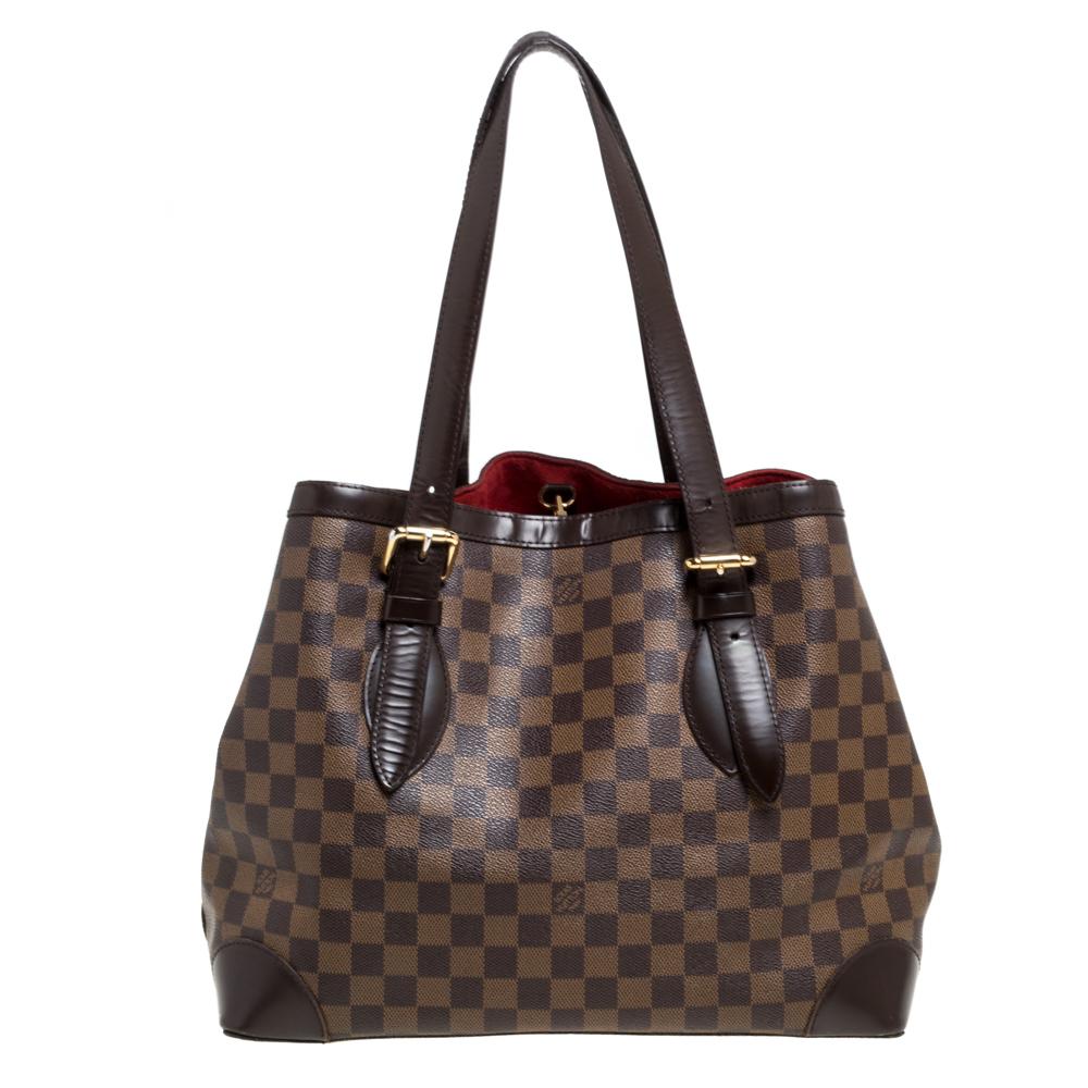Handbags from Louis Vuitton enjoy widespread popularity owing to their high style and functionality. This Hampstead bag, is no exception. Crafted from their signature Damier Ebene coated canvas, the bag comes with two flat top handles and a hook