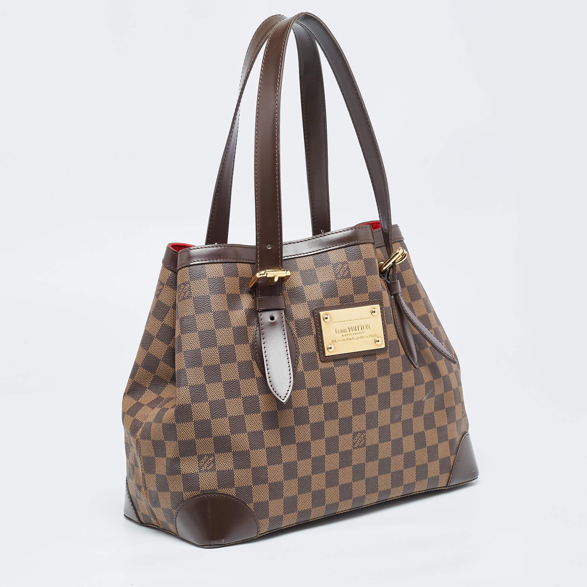 Handbags from Louis Vuitton enjoy widespread popularity owing to their high style and functionality. This Hampstead bag is no exception. Crafted from their signature Damier Ebene canvas, the bag comes with two flat top handles and a hook clasp that