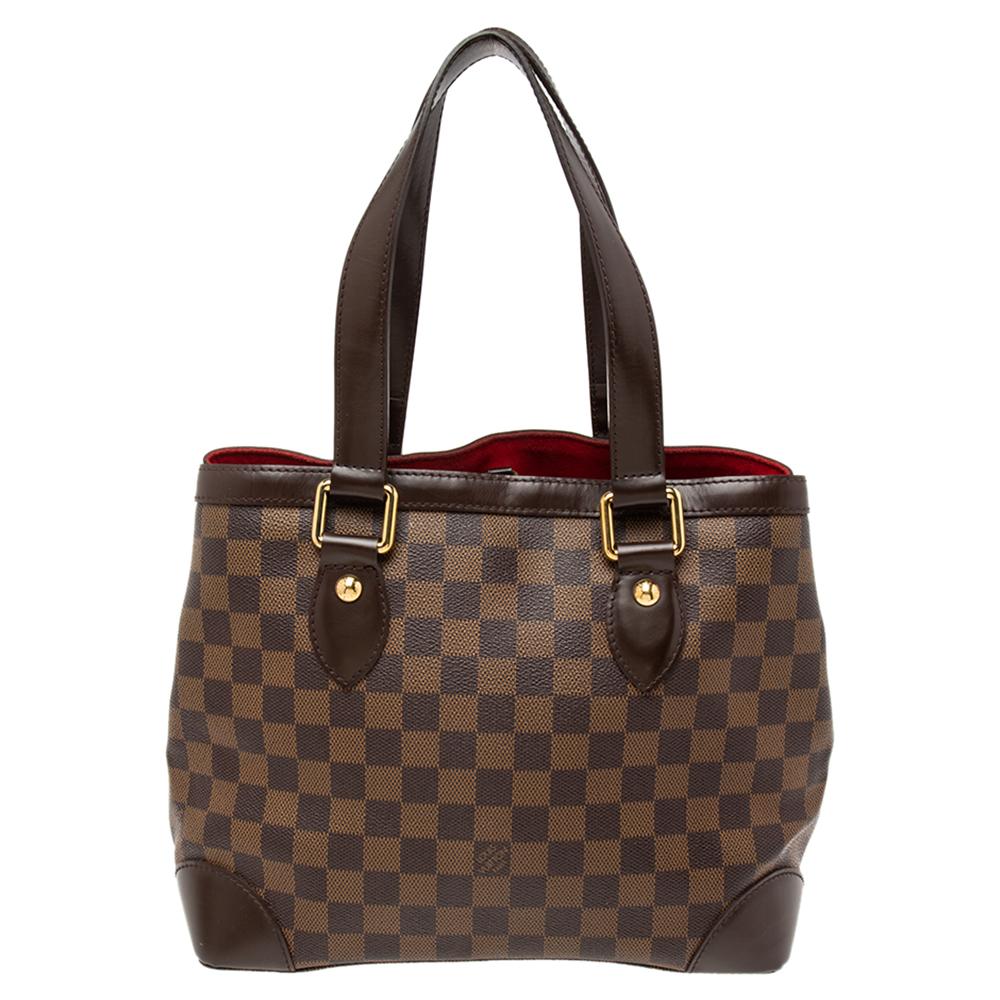 Handbags from Louis Vuitton enjoy widespread popularity owing to their high style and functionality. This Hampstead bag, is no exception. Crafted from their signature Damier Ebene canvas, the bag comes with two flat top handles and a hook clasp that