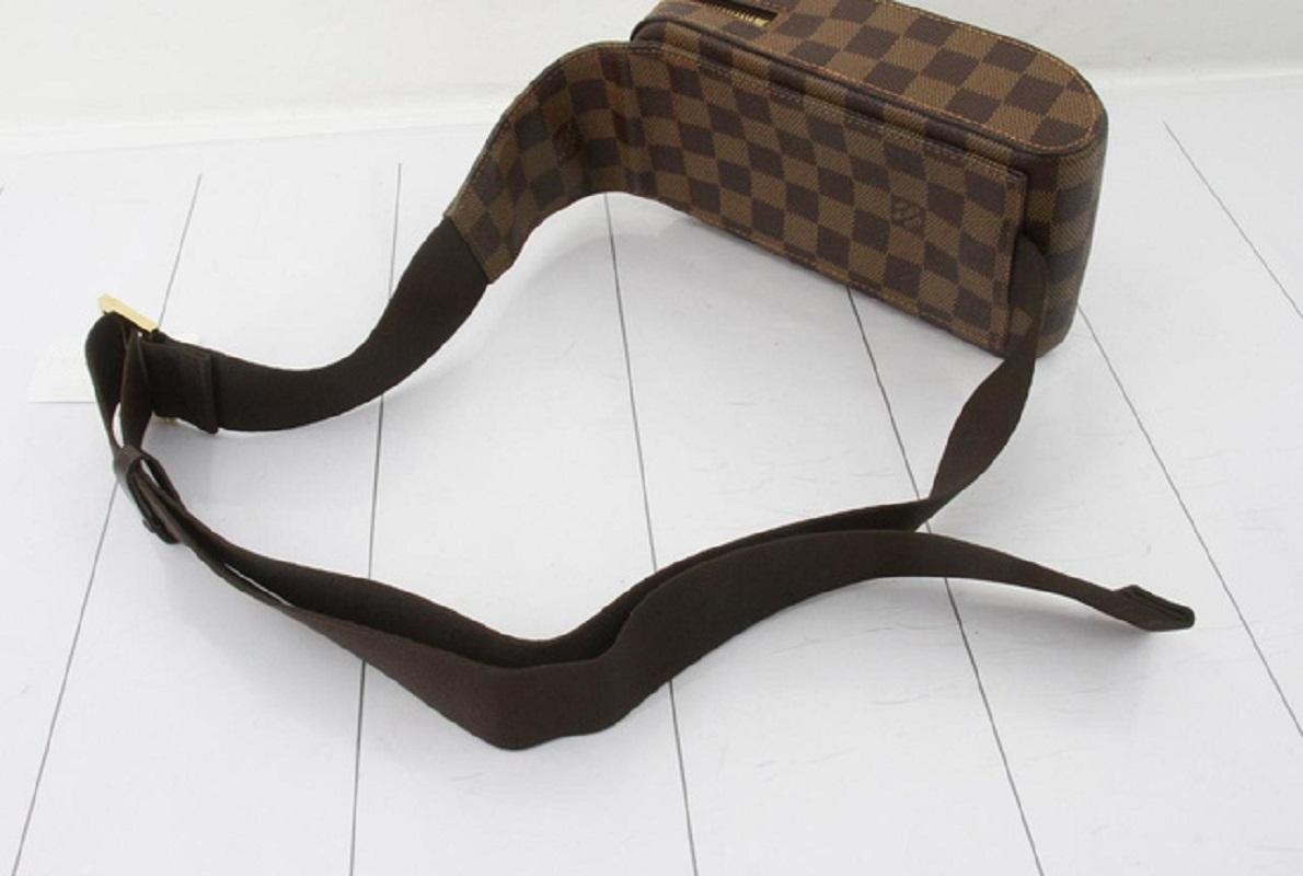 Brown and tobacco Damier Ebene coated canvas Louis Vuitton Geronimos waist bag with gold-tone hardware, single adjustable waist strap with buckle closure, single pocket at exterior with snap closure, red canvas lining and zip around closure.

