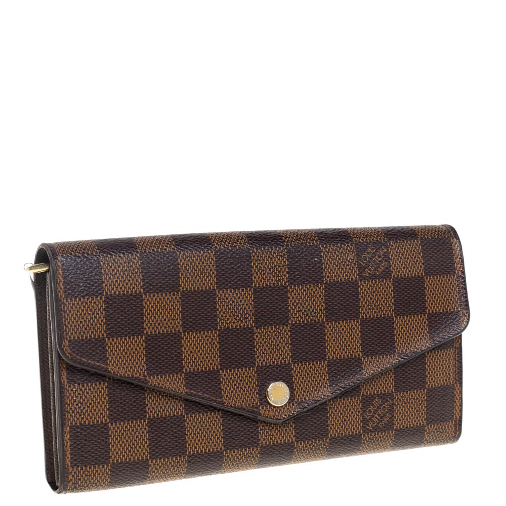 One of the most famous wallets by Louis Vuitton is the Sarah. This one here comes made from Damier Ebene coated canvas and the button on the flap opens to an interior with multiple card slots and a zip pocket. Perfect in size, this wallet can easily