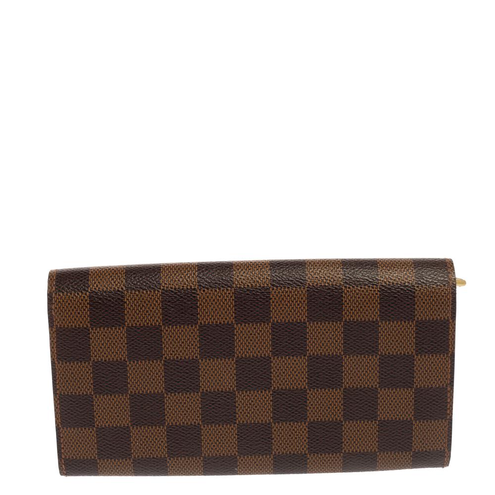 One of the most beloved and recognized accessories from the House of Louis Vuitton is this Sarah wallet. It is created using the Damier Ebene canvas on the exterior. It flaunts a gold-toned accent on the front and is provided with a leather-lined