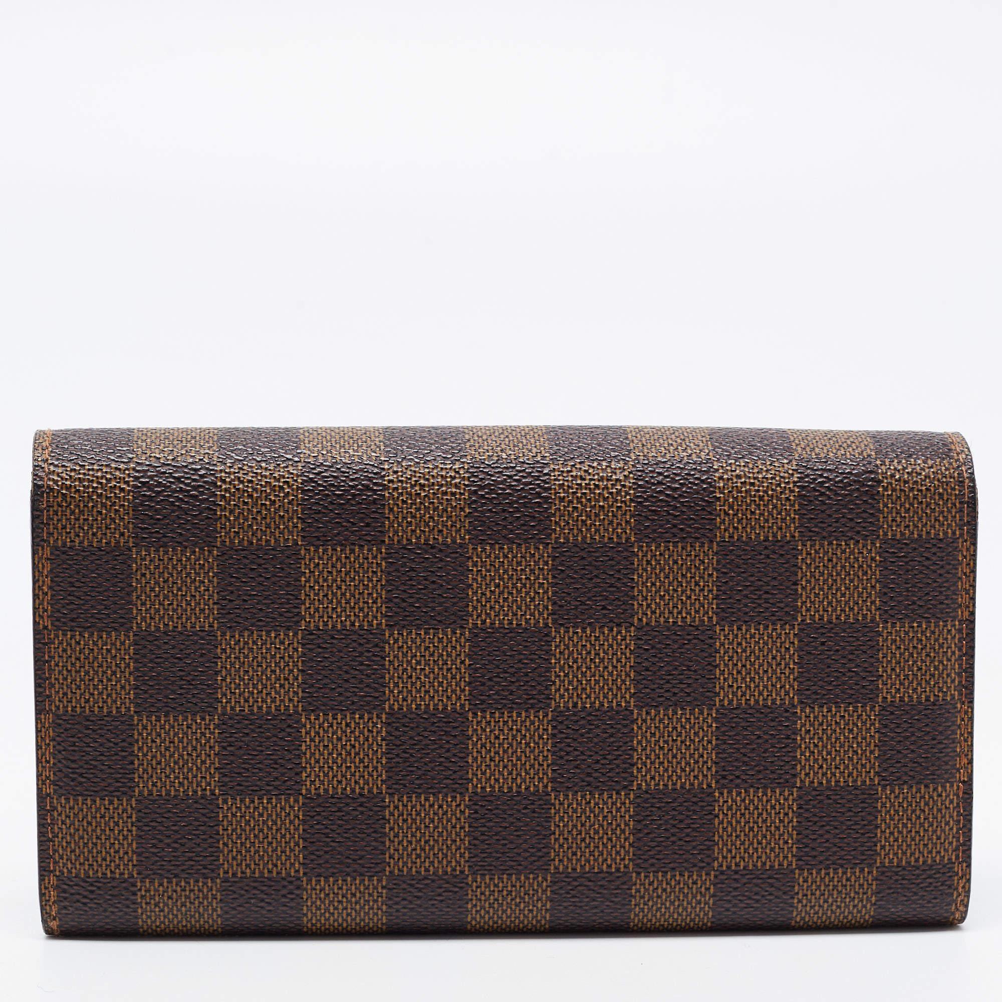 Crafted from the signature Damier Ebene canvas, this Louis Vuitton Sarah wallet is a valuable accessory. Its compartmentalized interior is perfect to store your monetary essentials, and the gold-tone accents add to the charm of the wallet.

