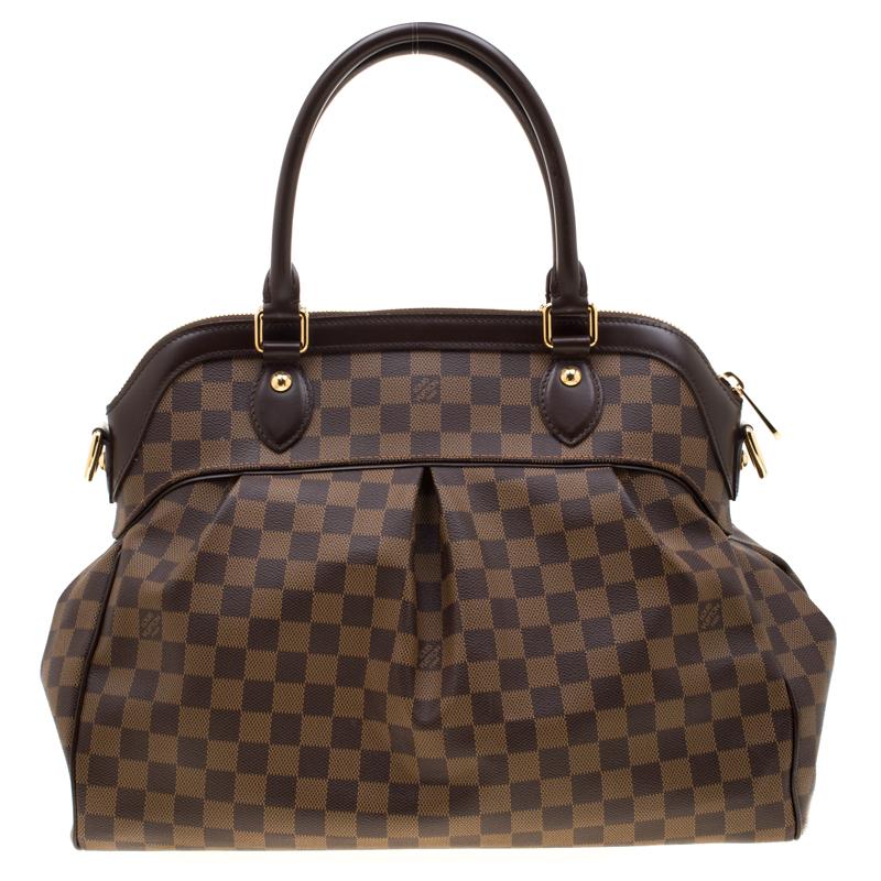 This Trevi bag by Louis Vuitton has been crafted from Damier Ebene canvas and it features two leather handles and a removable shoulder strap. It has gold-tone hardware, protective metal feet and a top zip that opens up to a spacious Alcantara