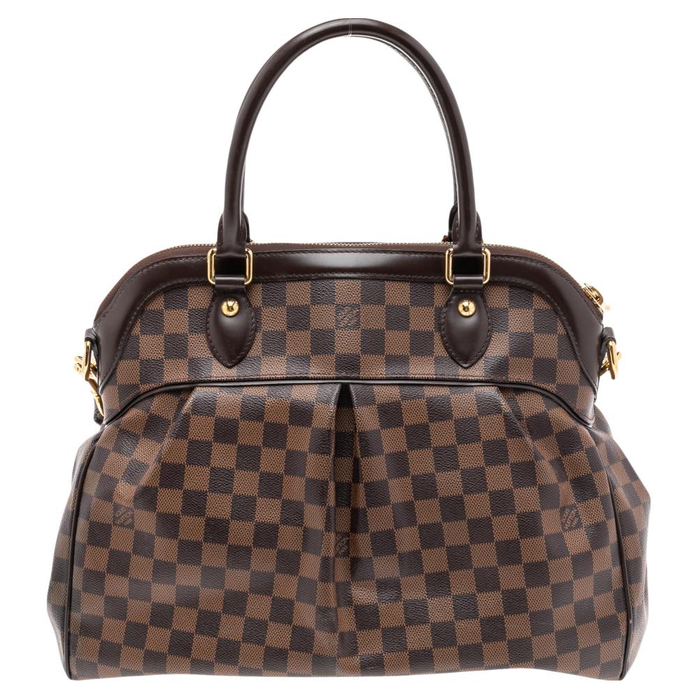 This Trevi bag by Louis Vuitton has been crafted from Damier Ebene canvas and it features two leather handles. It has gold-tone hardware, protective metal feet, and a top zip that opens up to a spacious Alcantara compartment. This finely-made piece