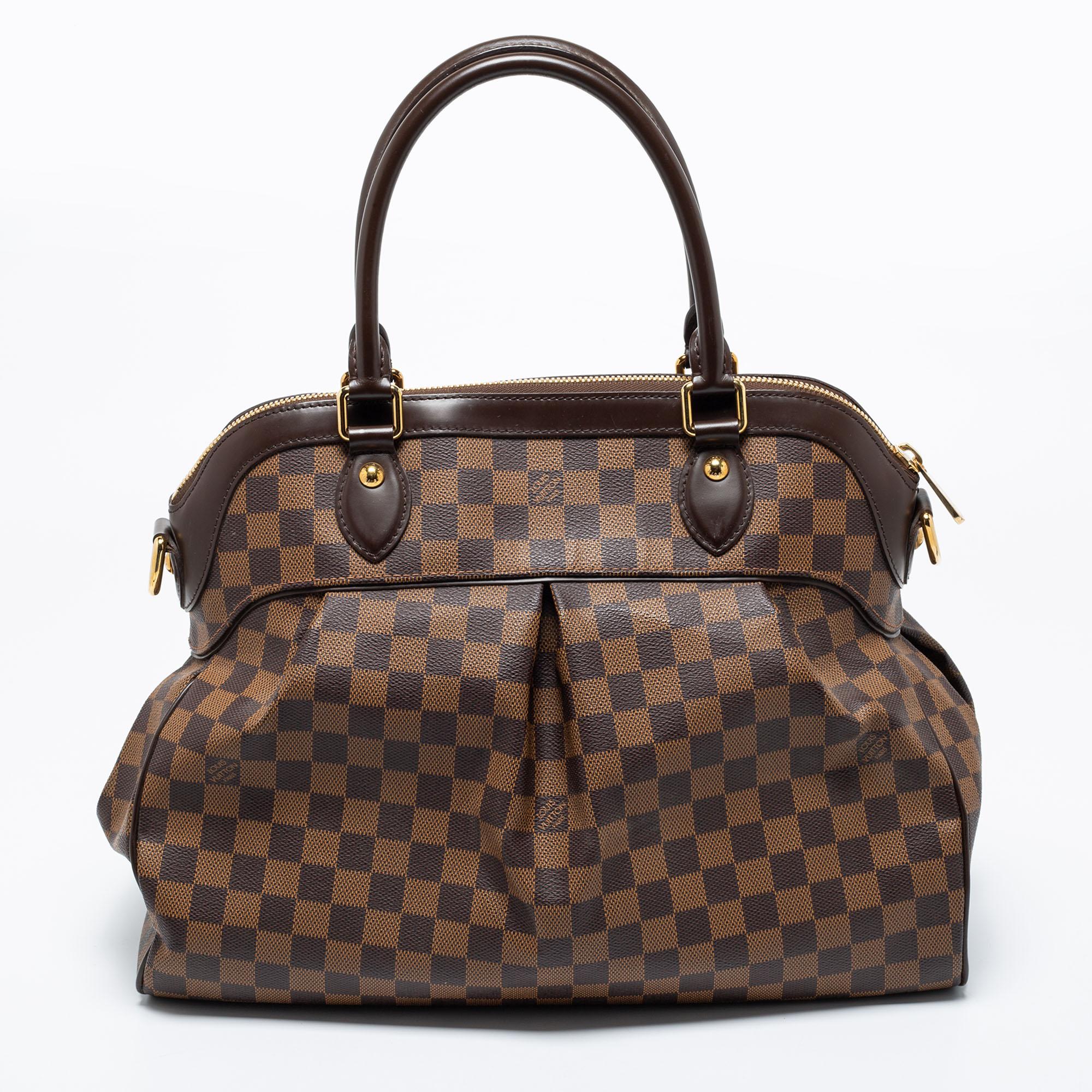 This Trevi bag by Louis Vuitton has been crafted from Damier Ebene canvas and it features two leather handles. It has gold-tone hardware, protective metal feet, and a top zip that opens up to a spacious Alcantara compartment. This finely-made piece