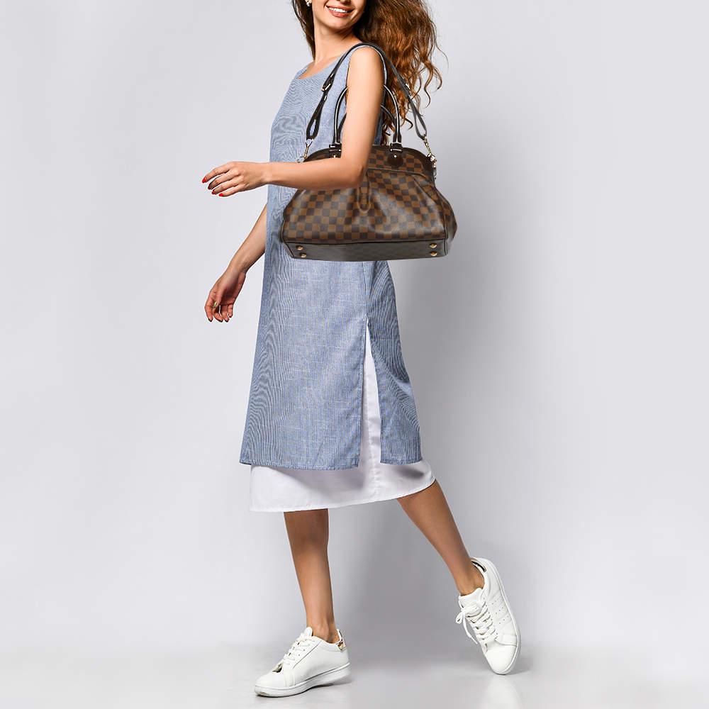 This pre owned Trevi bag by Louis Vuitton is crafted from Damier Ebene canvas and it features two leather handles and an optional bag strap. It has gold tone hardware protective metal feet and a top zip that opens to a spacious Alcantara