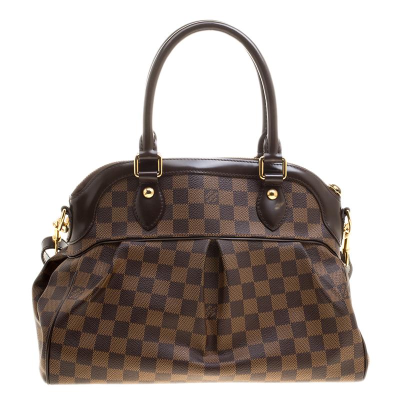 This Trevi PM bag by Louis Vuitton has been crafted from Damier Ebene canvas and it features two leather handles and a removable shoulder strap. It has gold-tone hardware, protective metal feet and a top zip that opens up to a spacious Alcantara
