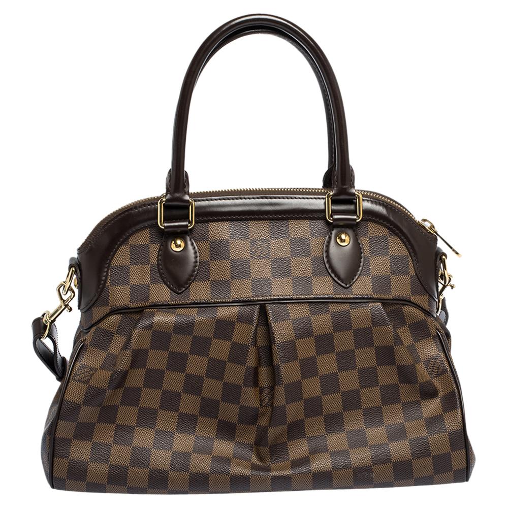 This Trevi bag by Louis Vuitton has been crafted from Damier Ebene coated canvas and it features two leather handles and a removable shoulder strap. It has gold-tone hardware, protective metal feet, and a top zip that opens up to a spacious