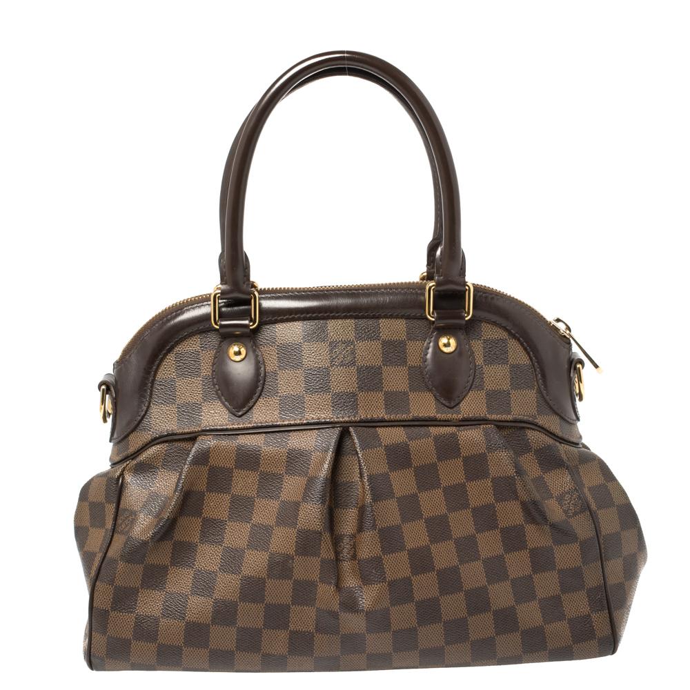 This Trevi bag by Louis Vuitton has been crafted from the signature Damier Ebene canvas and leather and it features two handles and a removable shoulder strap. It has gold-tone hardware, protective metal feet, and a top zipper that opens up to a