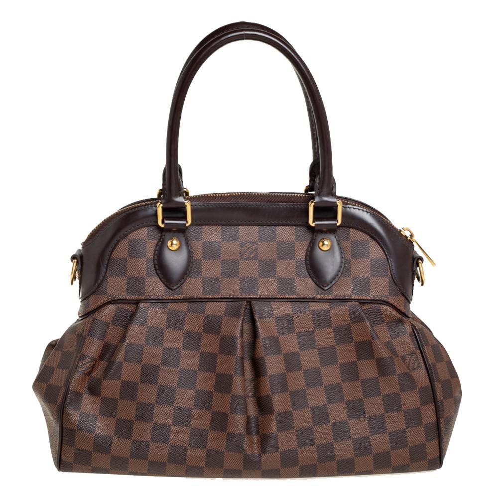 This Trevi bag by Louis Vuitton has been crafted from Damier Ebene canvas and it features two leather handles and a removable shoulder strap. It has gold-tone hardware, charms, protective metal feet, and a top zip that opens up to a spacious