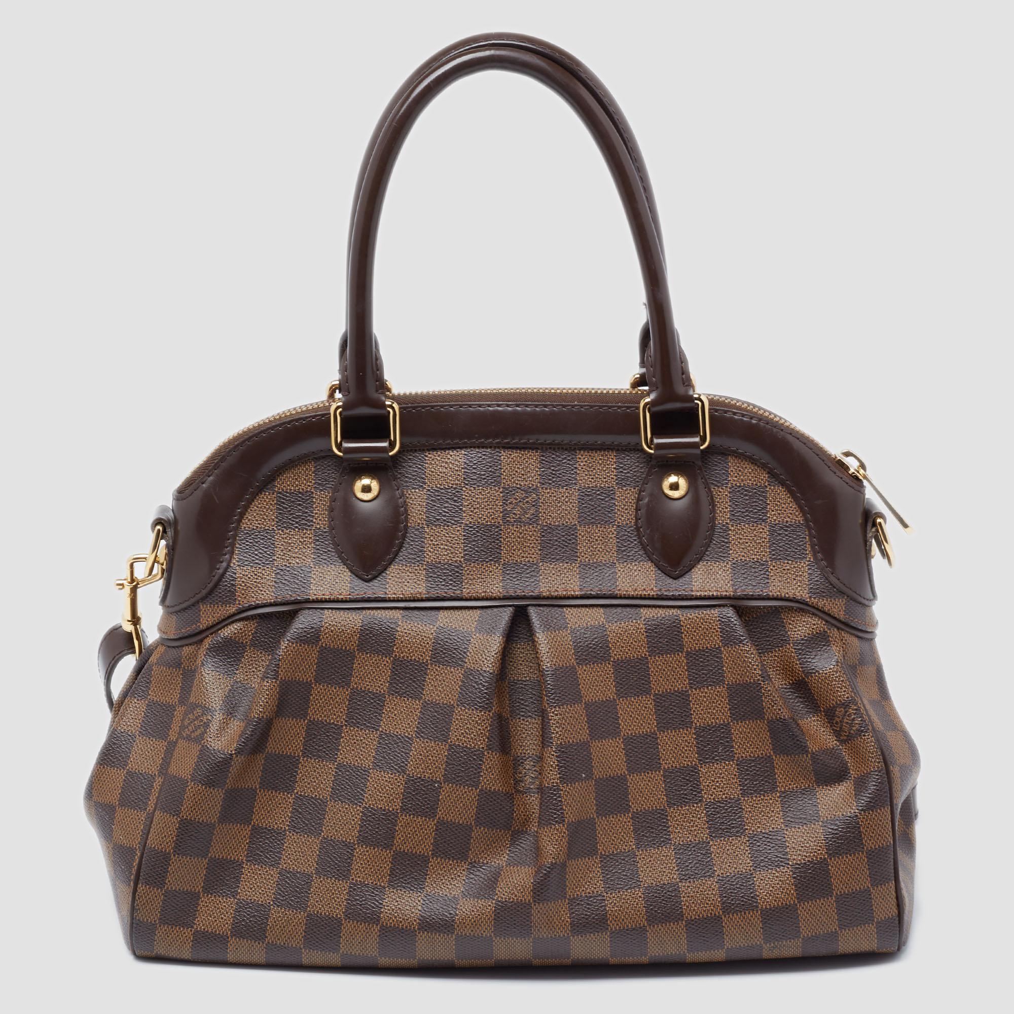This pre-owned Trevi bag by Louis Vuitton has been crafted from Damier Ebene coated canvas and it features two leather handles and an optional bag strap. It has gold-tone hardware, protective metal feet, and a top zip that opens up to a spacious