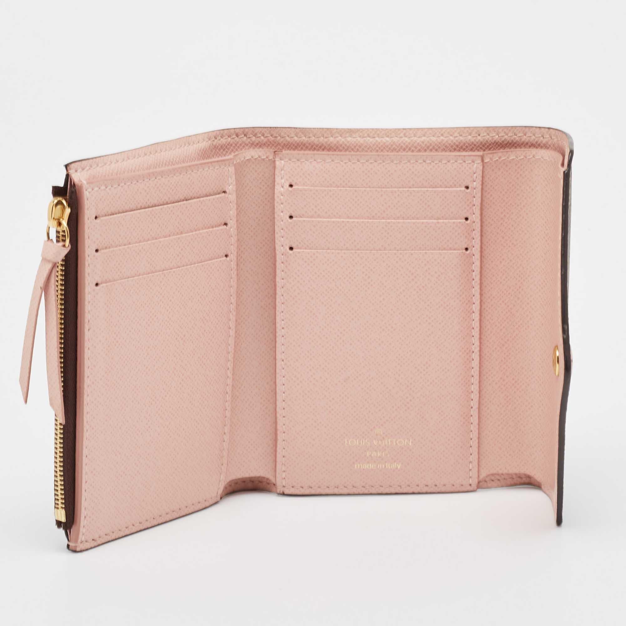 Basic essentials can be carried effortlessly in this Victorine wallet by Louis Vuitton. This compact wallet is crafted from the brands iconic Damier Ebene canvas with leather and pink lining. It offers quick and secure access to credit cards