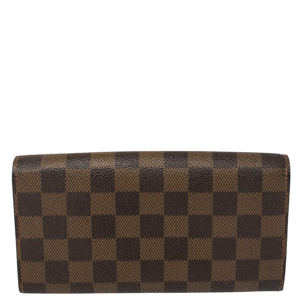 One of the most famous wallets by Louis Vuitton is the Sarah. This one here comes made from Damier Ebene canvas and the button on the flap opens to an interior with multiple card slots and a zip pocket. Perfect in size, this wallet can easily fit