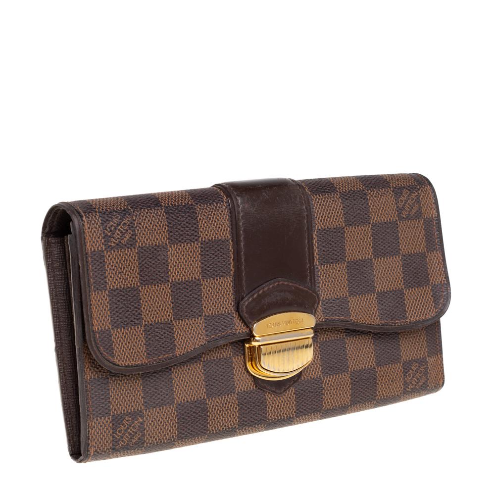 Carry this exquisite Damier Ebene Sistina wallet by Louis Vuitton in any one of your handbags. Crafted from canvas, it features a gold-tone lock on the flap. The interior features multiple card slots, two compartments for bills, two patch pockets,