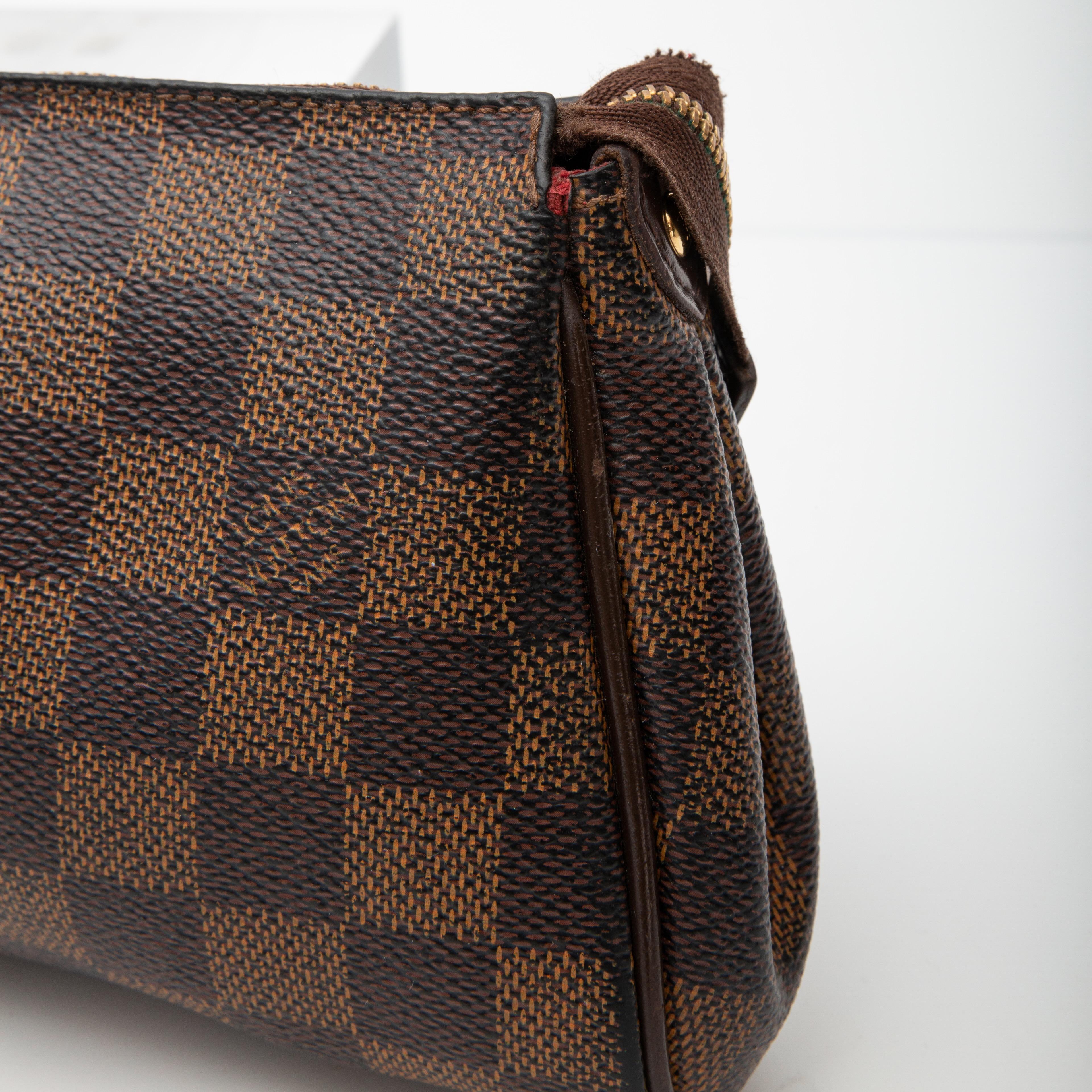 This pochette is constructed of coated canvas with LV's signature damier ebene print. Damier means checkerboard in French. This bag features a brass chain wrist strap, a detachable dark brown leather crossbody shoulder strap, top zip closure and a