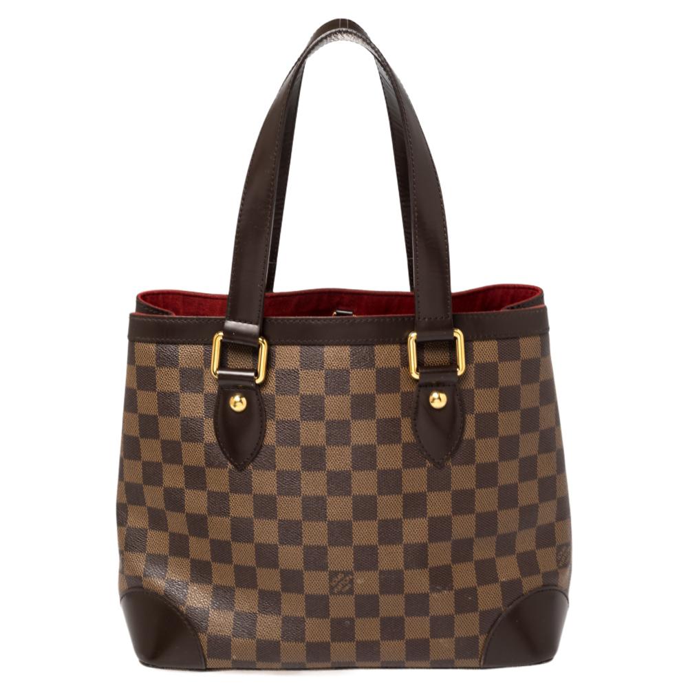 Handbags from Louis Vuitton enjoy widespread popularity owing to their high style and functionality. This Hampstead bag is no exception. Crafted from their signature Damier Ebene canvas, the bag comes with leather trims, two flat top handles, and a
