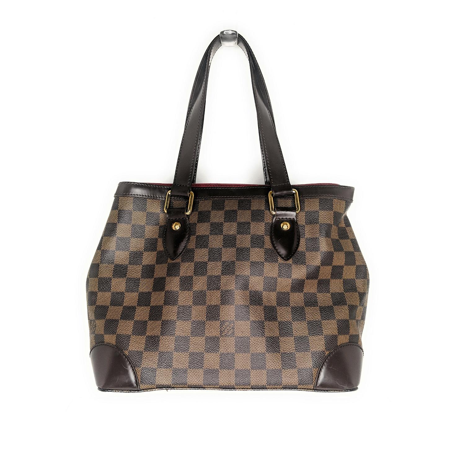 This stylish tote is finely crafted of Louis Vuitton signature damier check canvas. The shoulder bag features chocolate brown tall leather handles, reinforced base corners, and trim with polished brass hardware. The top of the bag is open to a rouge
