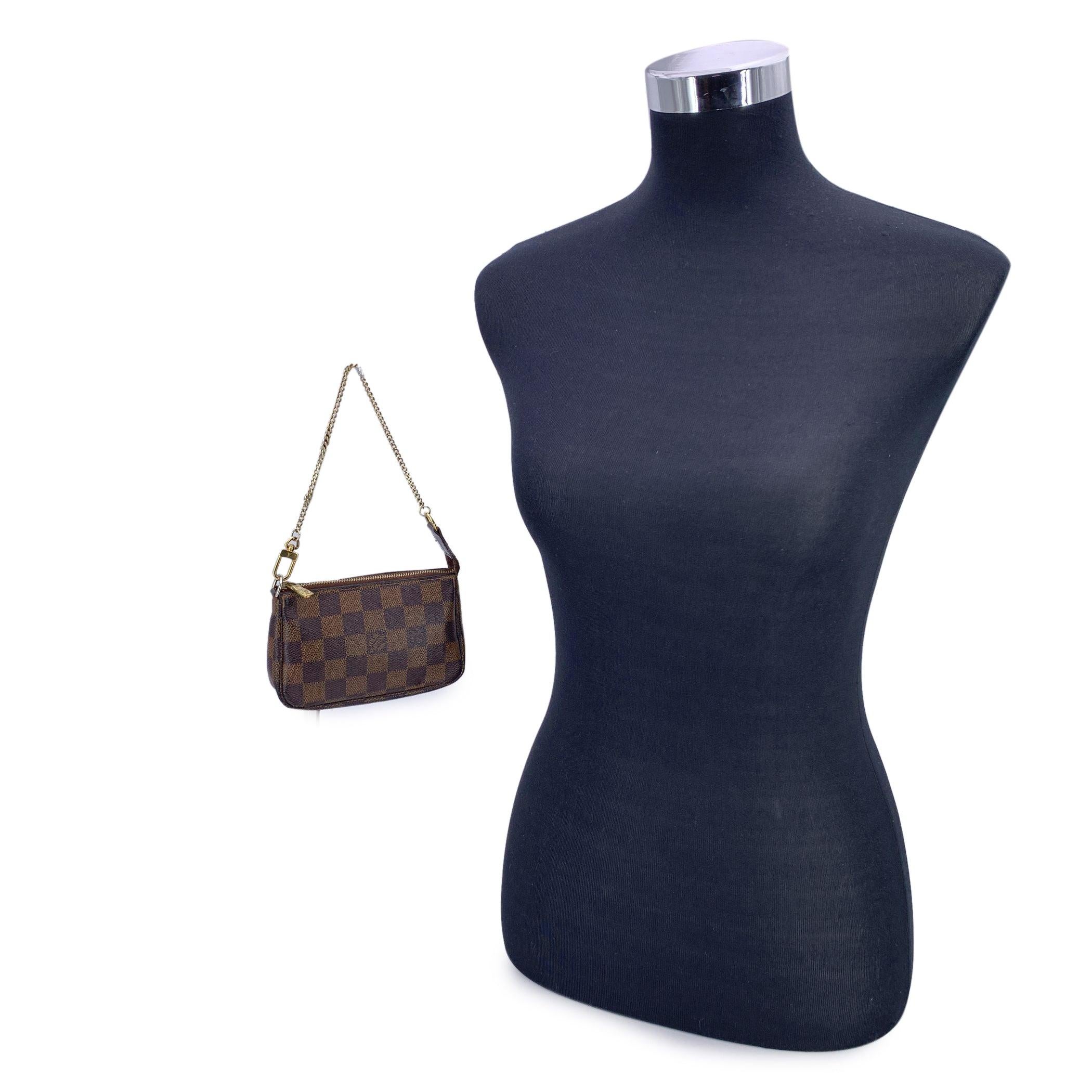 Introducing the Louis Vuitton Mini Pochette Accessoires, a compact and versatile piece that's perfect for those who appreciate luxury in even the smallest details. Crafted in Louis Vuitton's signature brown Damier Ebene canvas, this charming mini