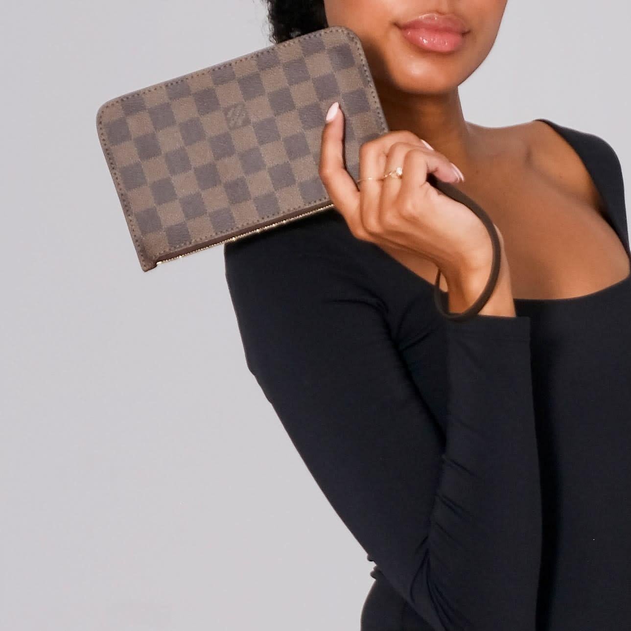 This pouch bag is Damier coated canvas and it features a brown leather wristlet strap, gold tone hardware, top zip closure, and a red striped fabric interior with a patch pocket.  Retail.

Color: Brown Damier ebene print
Material: Coated canvas with