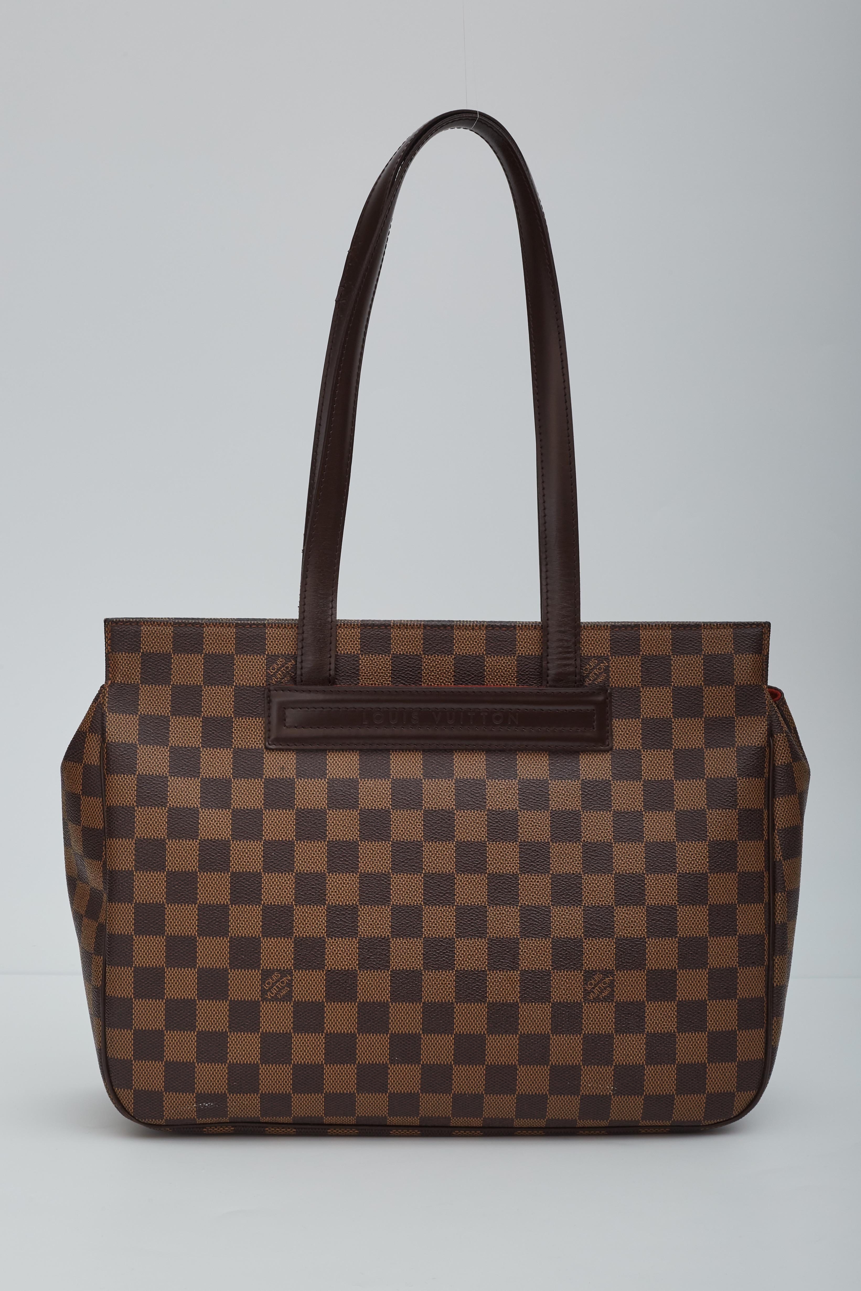 This bag is made with signature damier ebène coated canvas canvas. The bag features dual long top handles, a top that opens and snaps back to place and brown leather trim. the interior is finished with red woven fabric lining with slip pockets.
