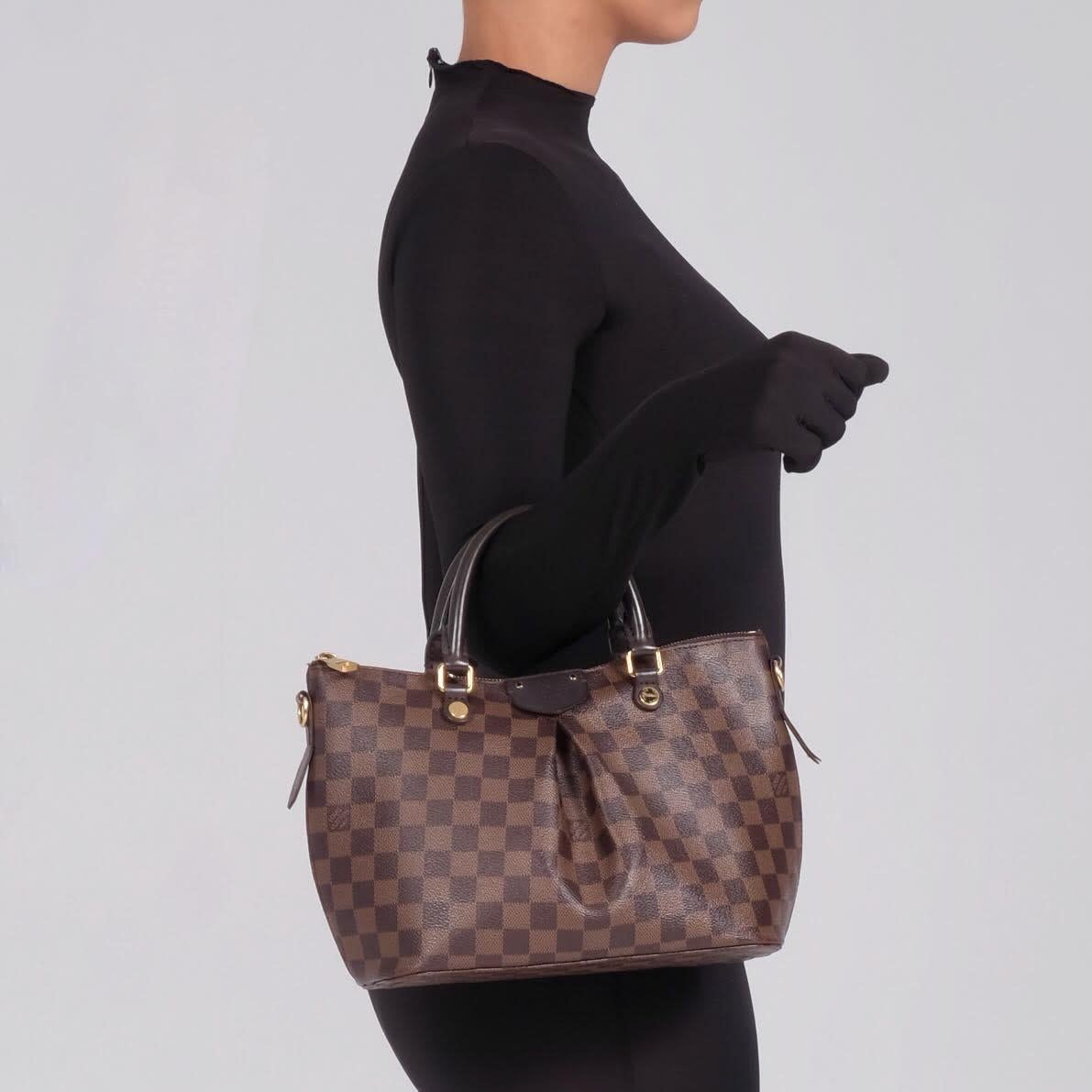 This bag made of Louis Vuitton Damier on pleated, coated canvas in brown. The bag features chocolate brown leather trim, dual rolled top leather top handles, and an optional, adjustable shoulder strap with polished brass hardware. The top zipper