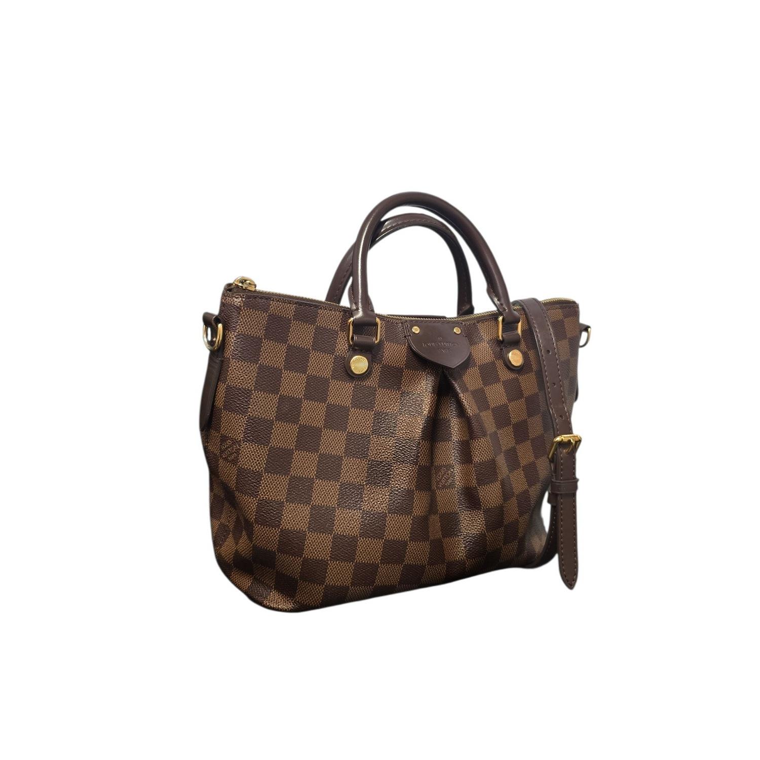 Este elegante bolso está confeccionado en lona a cuadros Damier de Louis Vuitton en marrón ebano. El bolso tiene un pliegue prominente en el centro, con asas superiores de piel enrolladas y una bandolera de piel de ebene; todo ello con detalles de